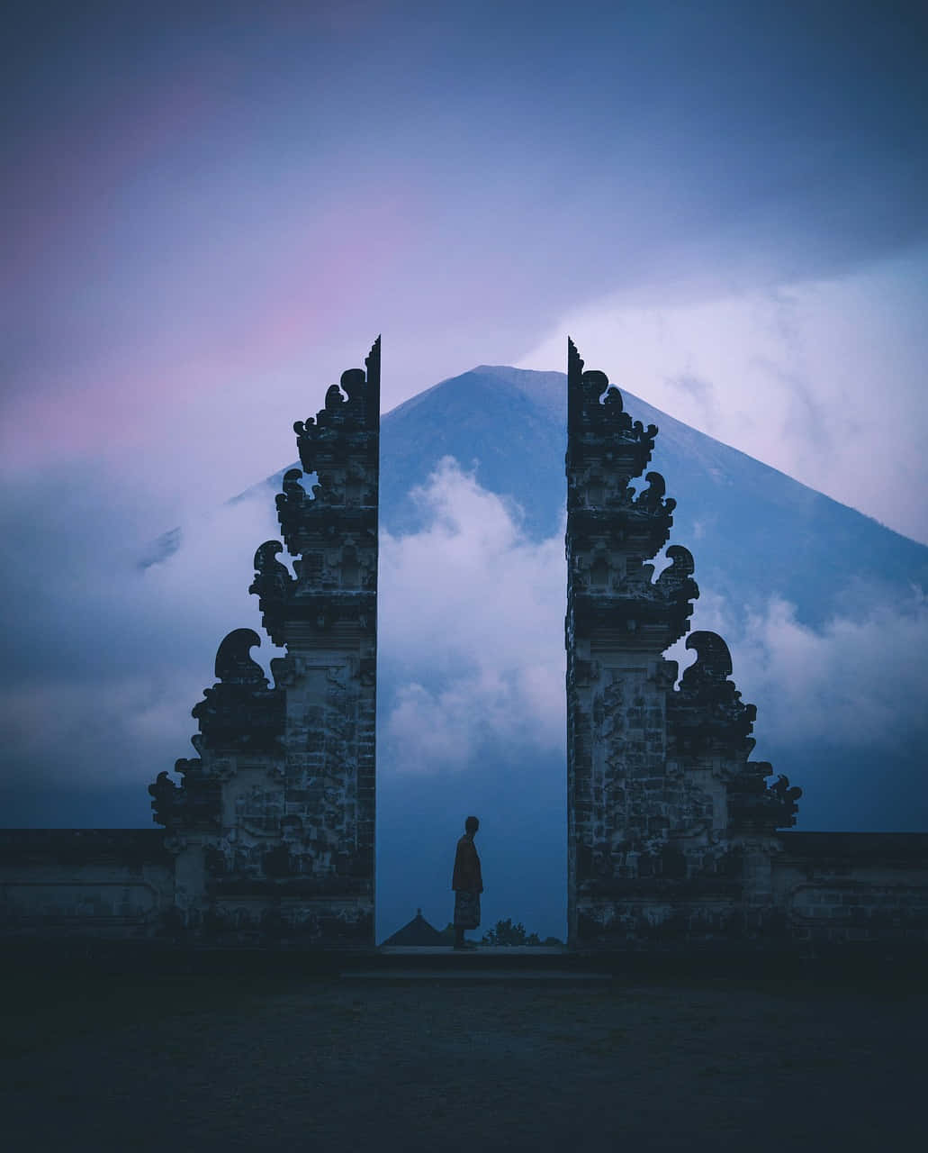 Beautiful Photography 桌布 壁紙 — 一個孤獨的身影站在裝飾石門之間，石門框住了暮色天空下霧氣繚繞的山巒。