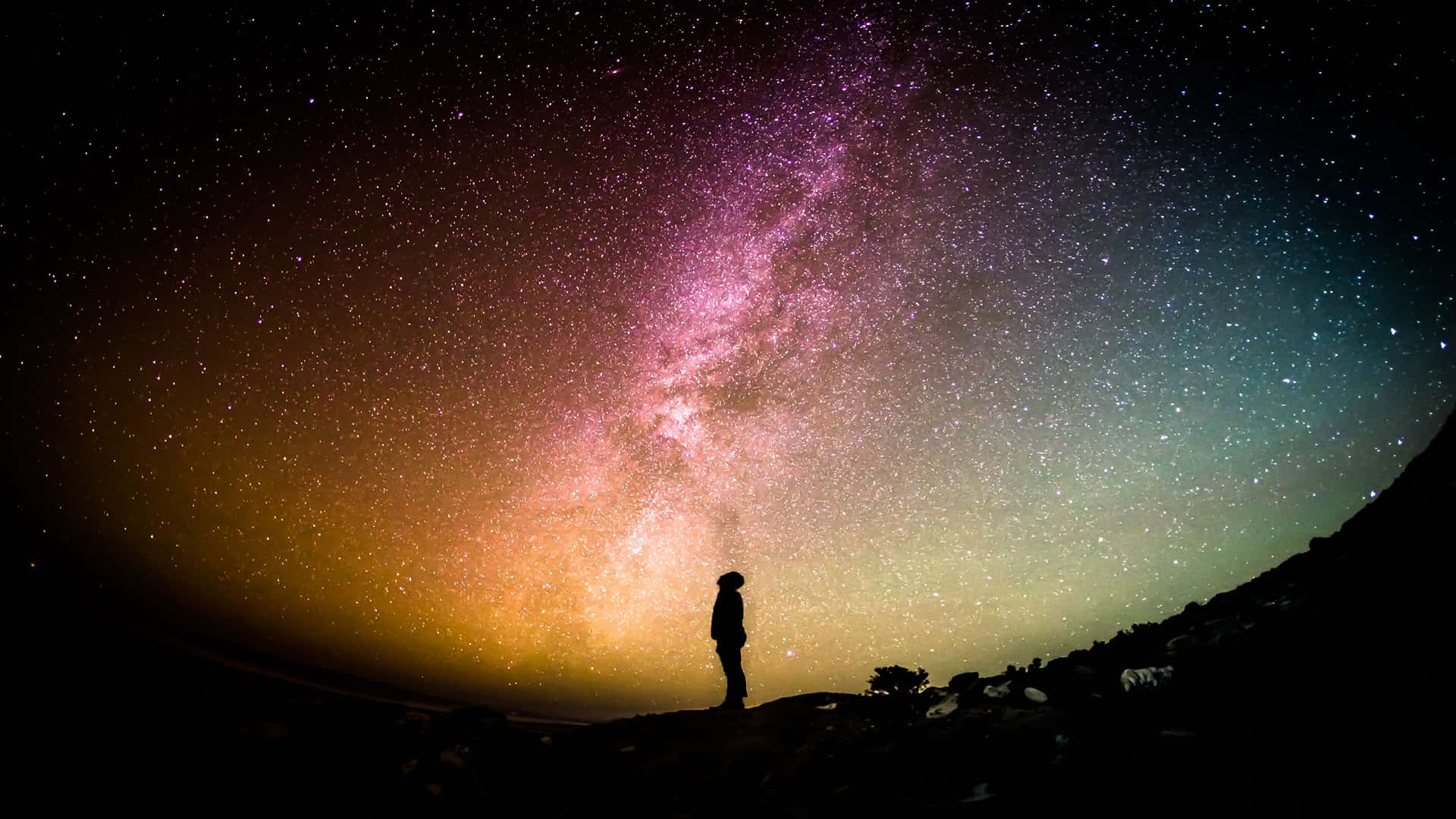 Eternal Life 桌布 壁紙 — 一個孤獨的身影站在黑暗的山丘上，仰望橫跨繁星夜空、色彩斑斕的壯麗銀河。