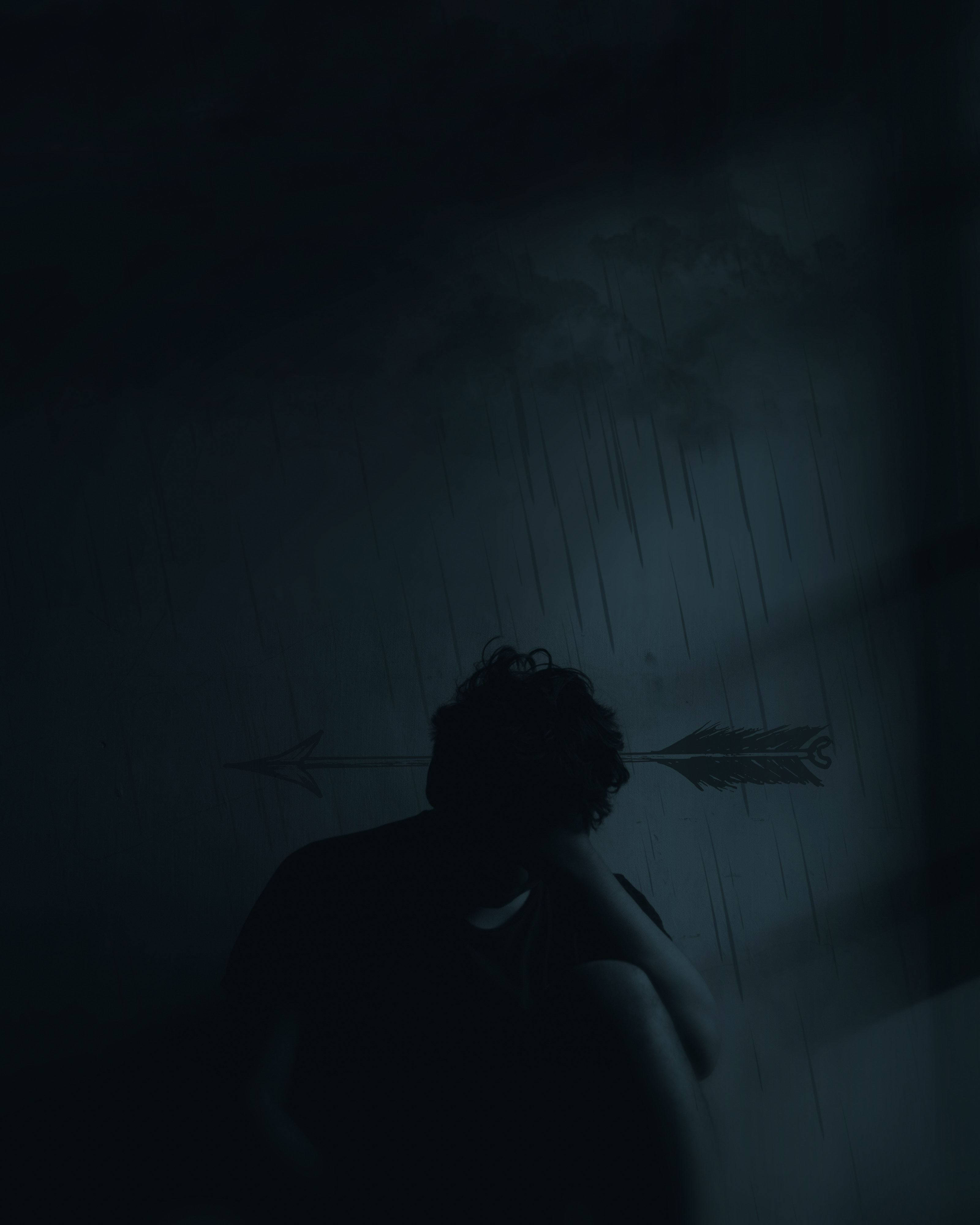 Dark Aesthetic iPhone 桌布 壁紙 — 一個孤獨的身影蜷縮在陰影中，雨水順著箭頭剪影後的窗戶流下。