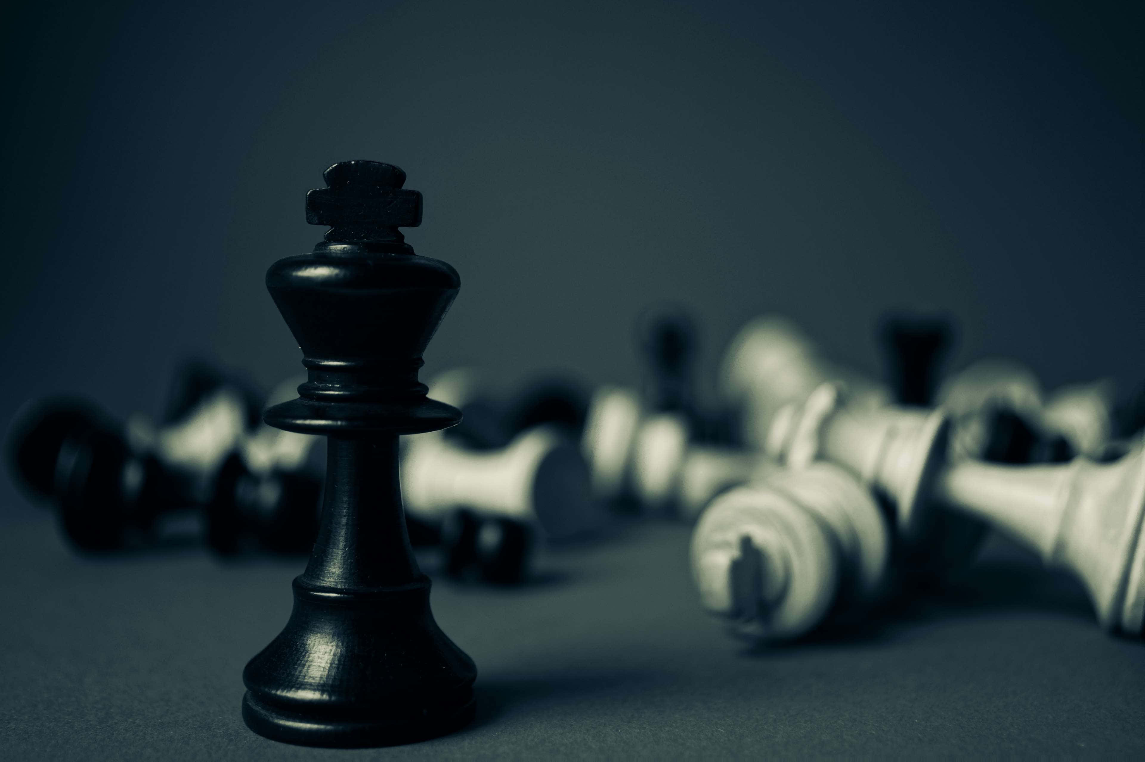 Black And White Chess 桌布 壁紙 — 一個孤獨的黑色國際象棋國王直立，而倒下的白色棋子散落在模糊的背景中。