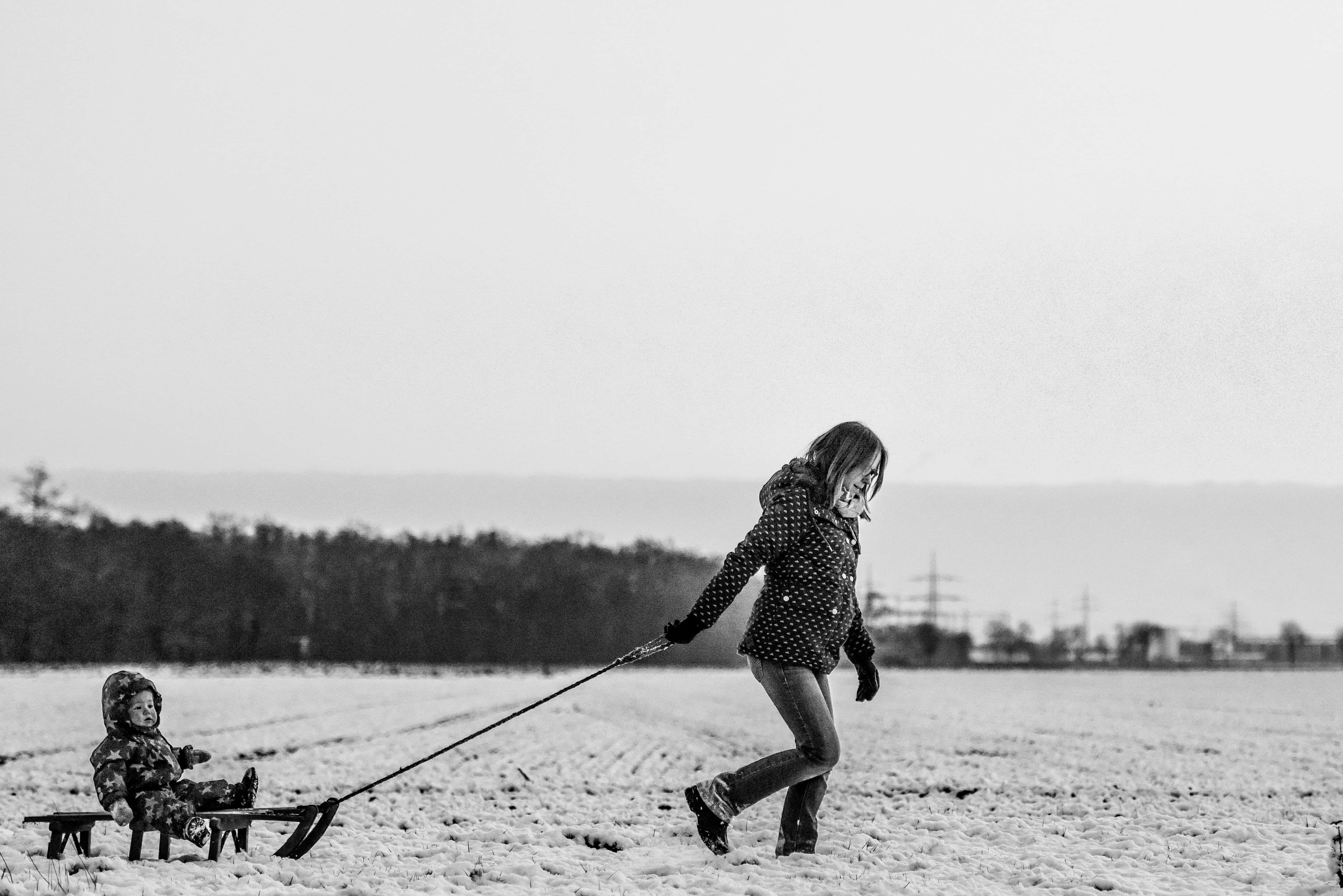媽媽 桌布 壁紙 — 一個孩子在陰天嘅雪地上拖住一個載有幼兒嘅雪橇。