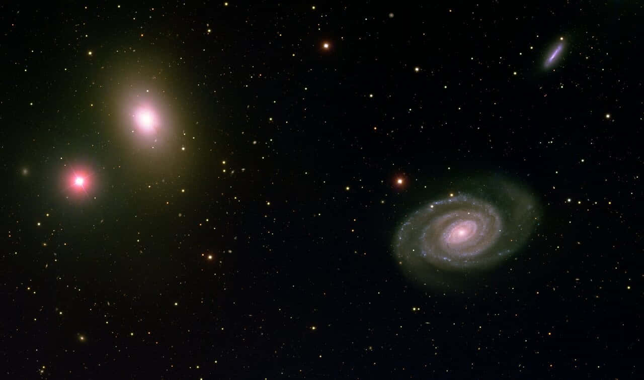 Elliptical Galaxy 桌布 壁紙 — 一個宇宙景觀，展示了一個帶有粉紅色核心和旋轉臂的螺旋星系，以及閃爍的星星在星場背景下。