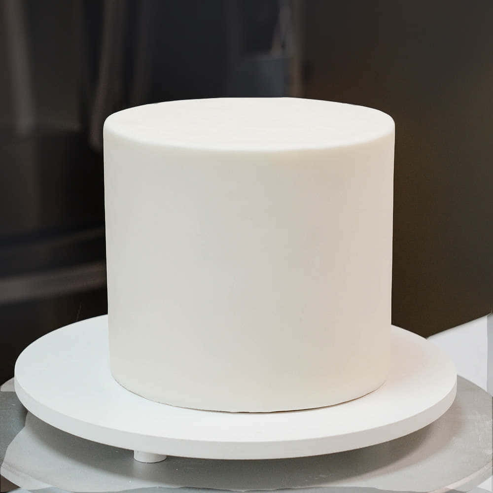 Cake Fondant 桌布 壁紙 — 一個完美無瑕的白色圓柱形蛋糕，表面覆蓋著光滑的翻糖，放在白色蛋糕架上，背景是深色模糊的。