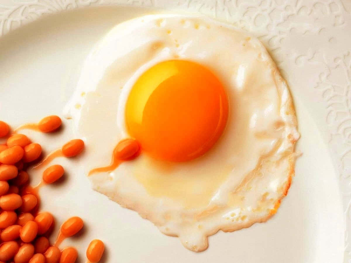 Egg White 桌布 壁紙 — 一個完美煎好的太陽蛋，帶有鮮豔的橙色蛋黃，放在一個華麗的白色碟子上，旁邊是亮橙色的豆子。