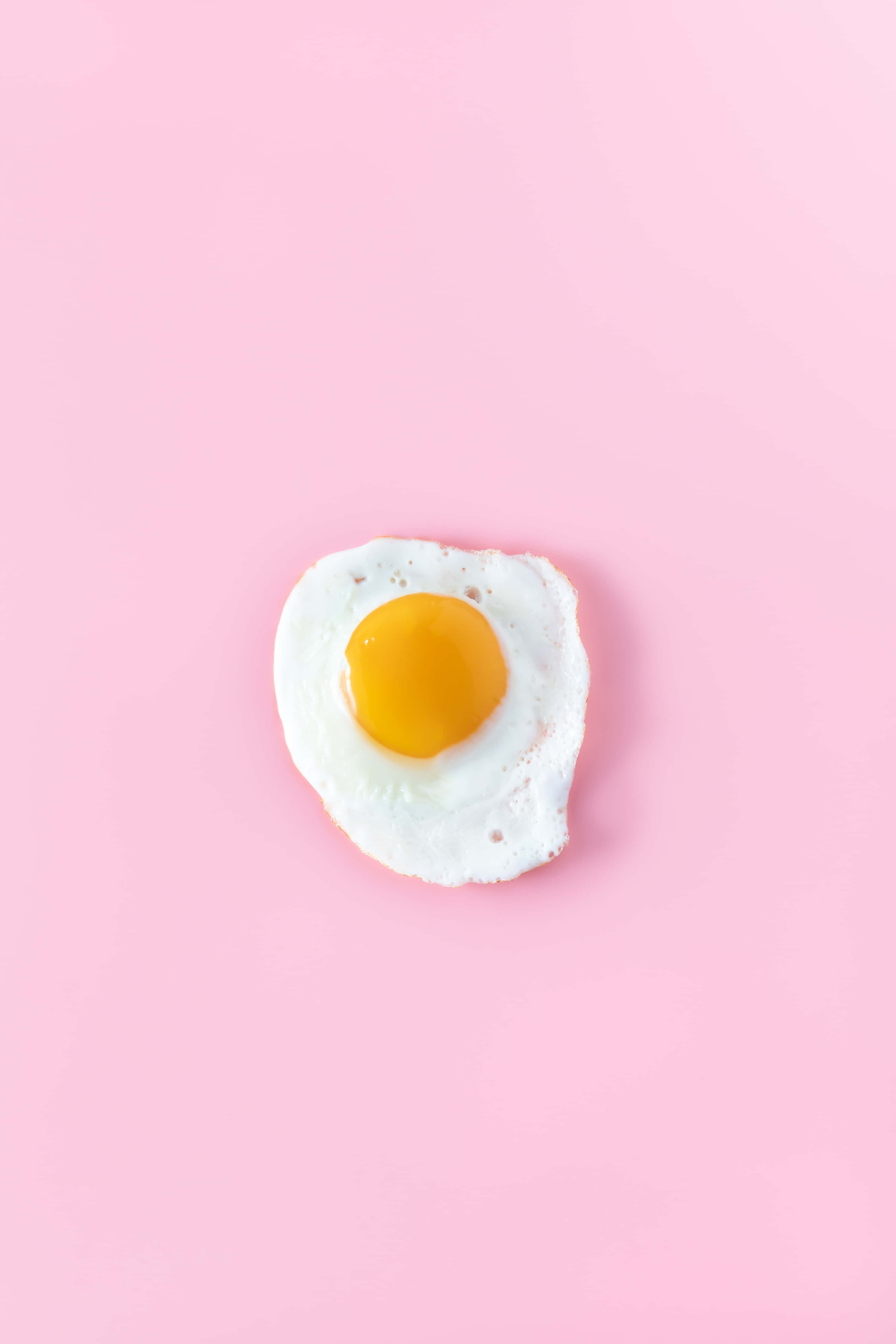 Egg White 桌布 壁紙 — 一個完美煎好的太陽蛋，置中於柔軟的粉紅色背景上，帶有鮮黃色的蛋黃。