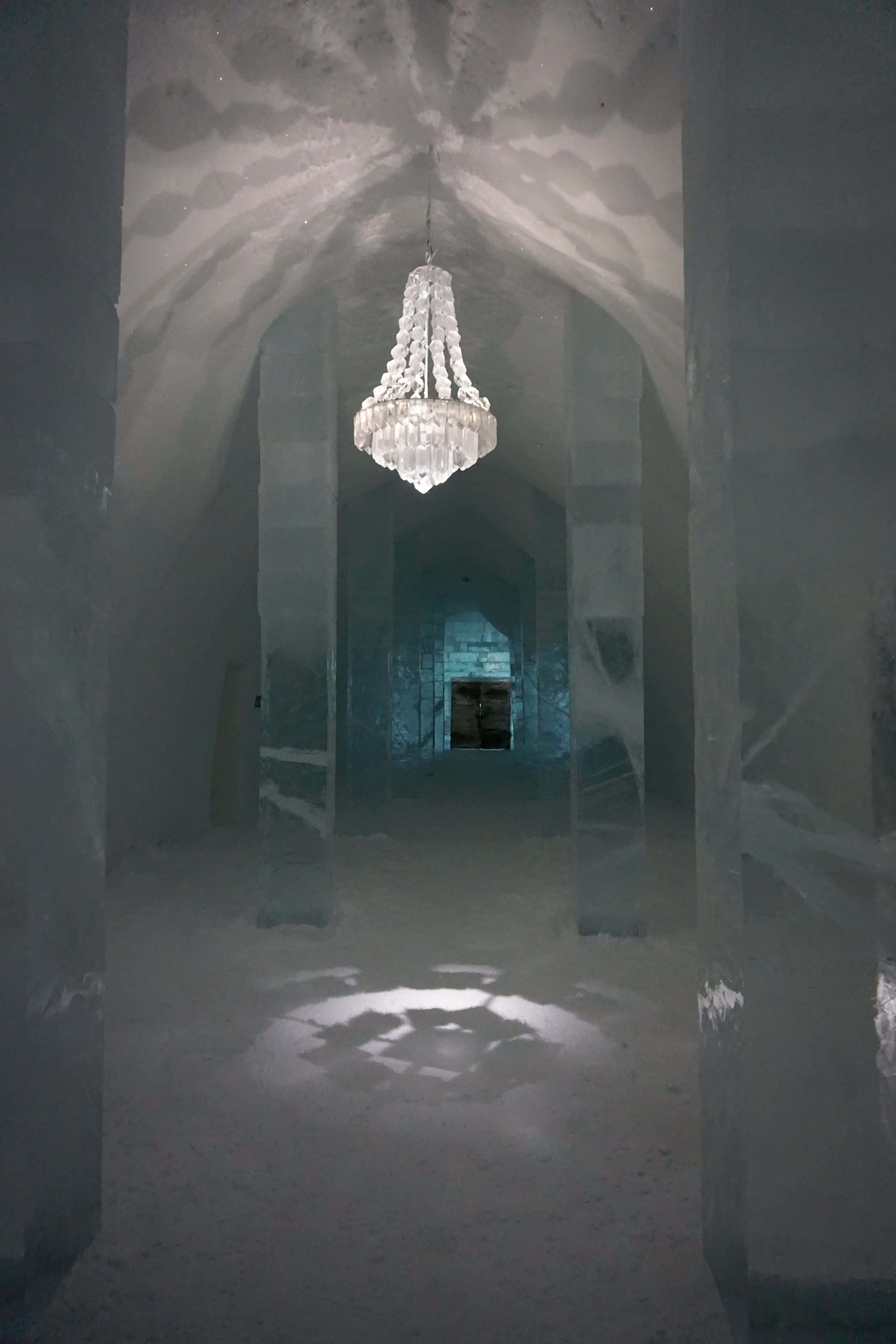 Ice Hotel 桌布 壁紙 — 一個宏偉的冰吊燈懸掛在一個像大教堂的冰凍走廊中，帶有拱形天花板和冰柱。