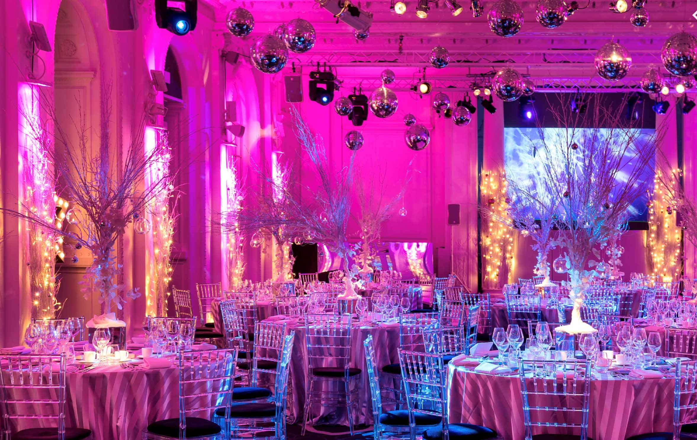 Corporate Event 桌布 壁紙 — 一個宏偉的宴會廳，沐浴在充滿活力的粉紅色和紫色燈光中，頭頂懸掛著迪斯科球，餐桌已為優雅的活動佈置好。
