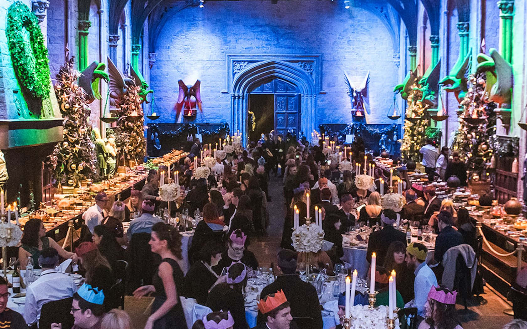 Harry Potter Christmas 桌布 壁紙 — 一個宏偉的宴會廳，賓客身著正裝，在藍色和綠色燈光以及龍裝飾下用餐。
