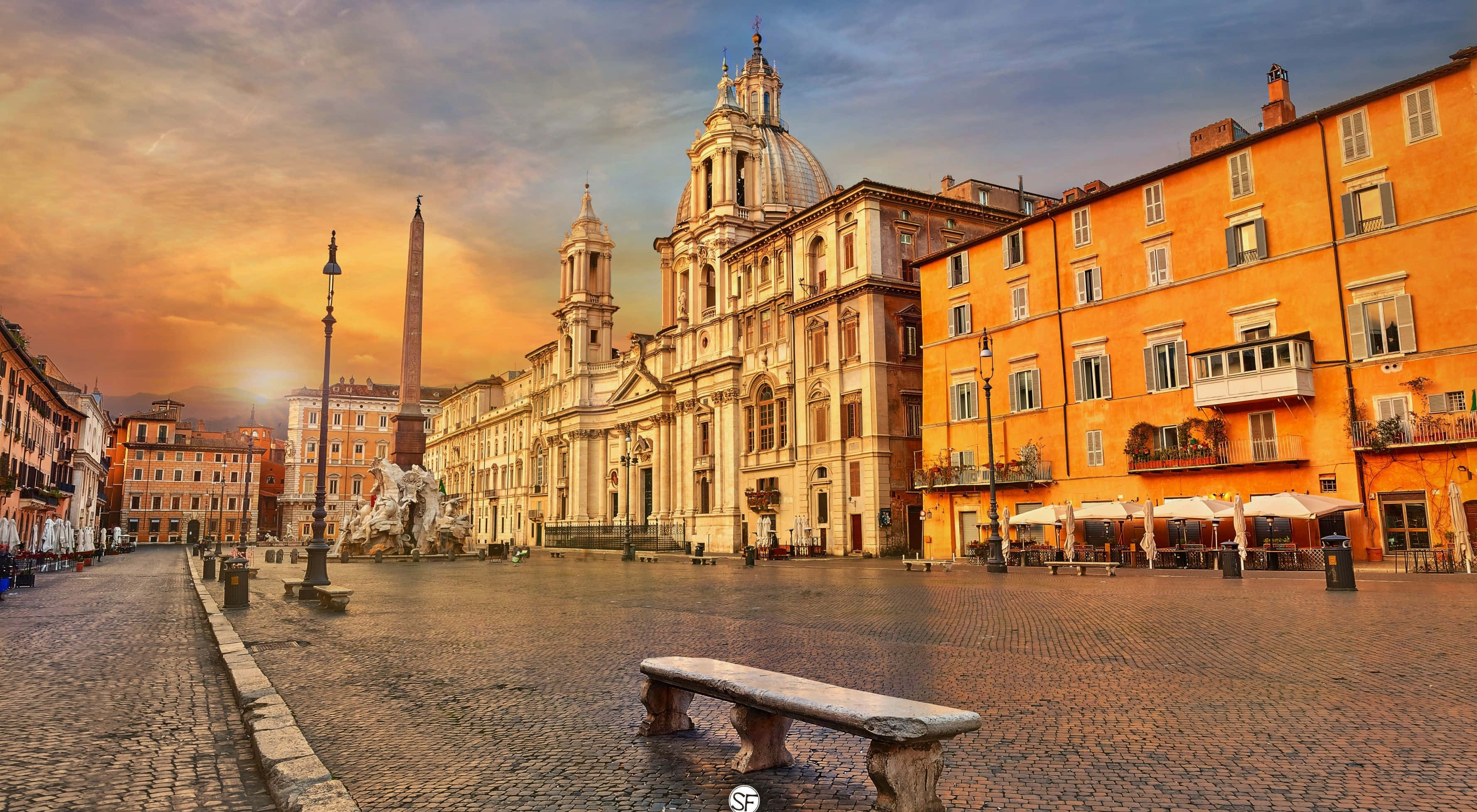 Rome 桌布 壁紙 — 一個宏偉的歐洲廣場沐浴在金黃色的日落光線中，前景有歷史建築、噴泉和石凳。