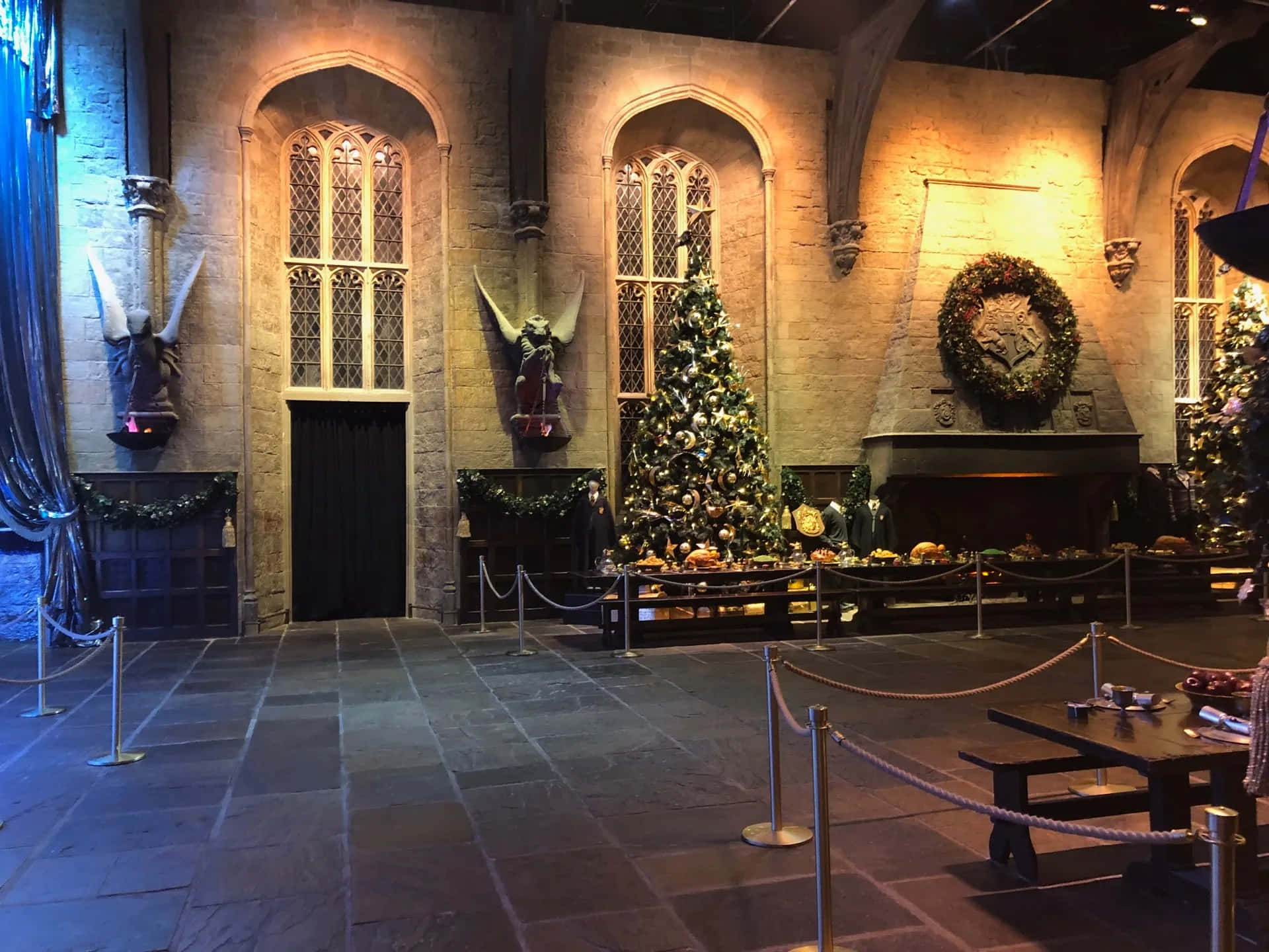 Harry Potter Christmas 桌布 壁紙 — 一個宏偉的石砌大廳，在溫暖的金色燈光下裝飾著節日聖誕樹和花環。