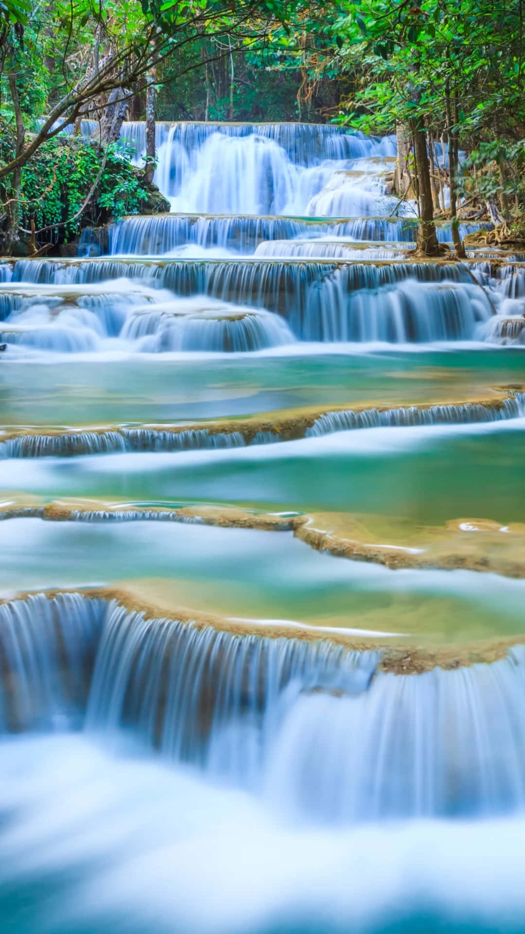 3d Waterfall 桌布 壁紙 — 一個寧靜的多層瀑布穿過茂密的綠色叢林，伴隨著碧綠色的水池和霧狀的白色水流。