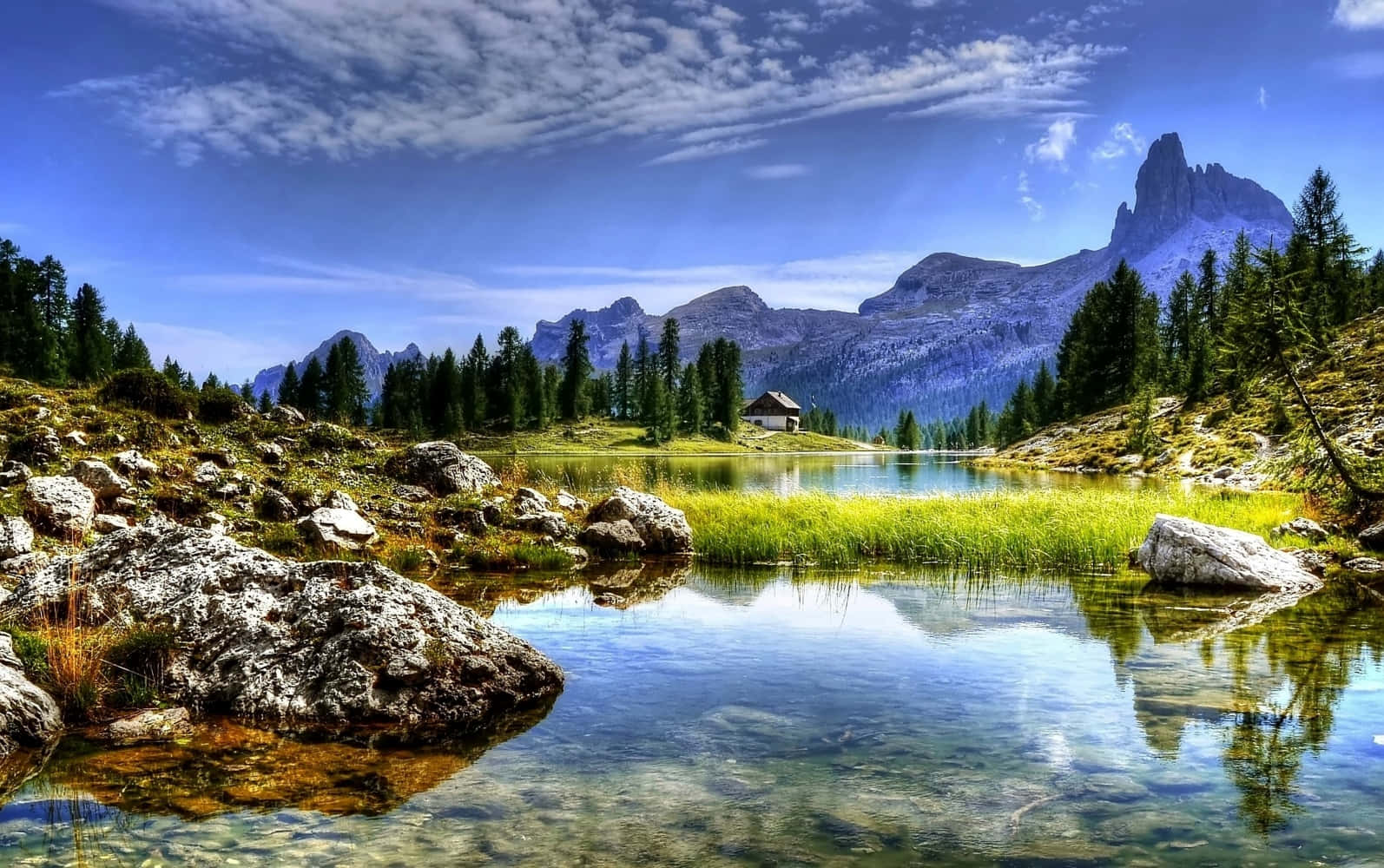 Beautiful Landscape 桌布 壁紙 — 一個寧靜的山間湖泊倒映著高聳的山峰和藍天，天空中有縷縷白雲，周圍環繞著松樹和岩石。
