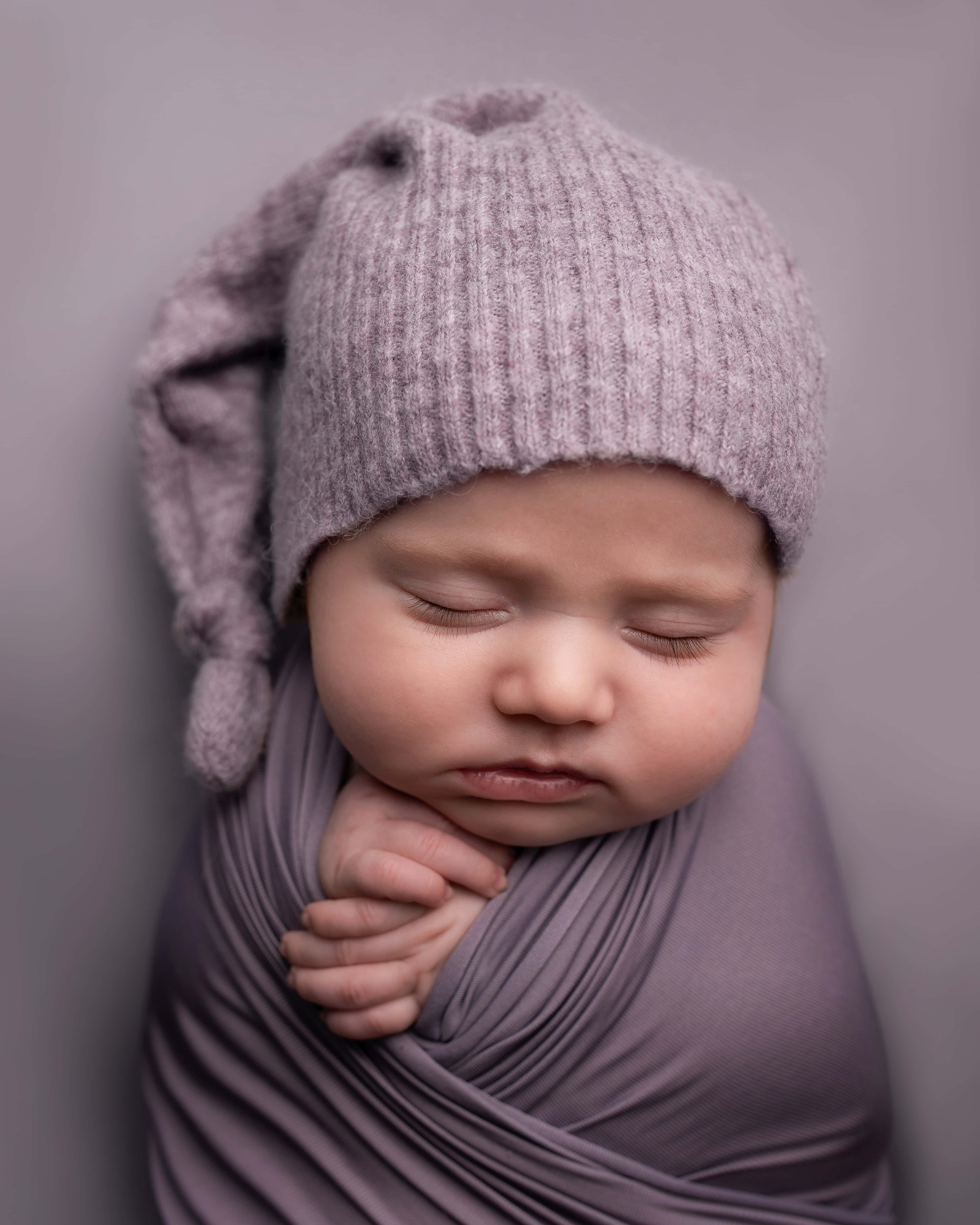 Baby Boy 桌布 壁紙 — 一個寧靜的新生嬰兒包裹在柔軟的薰衣草布料中，戴著相配的針織帽，在柔和的灰色背景下安然入睡。