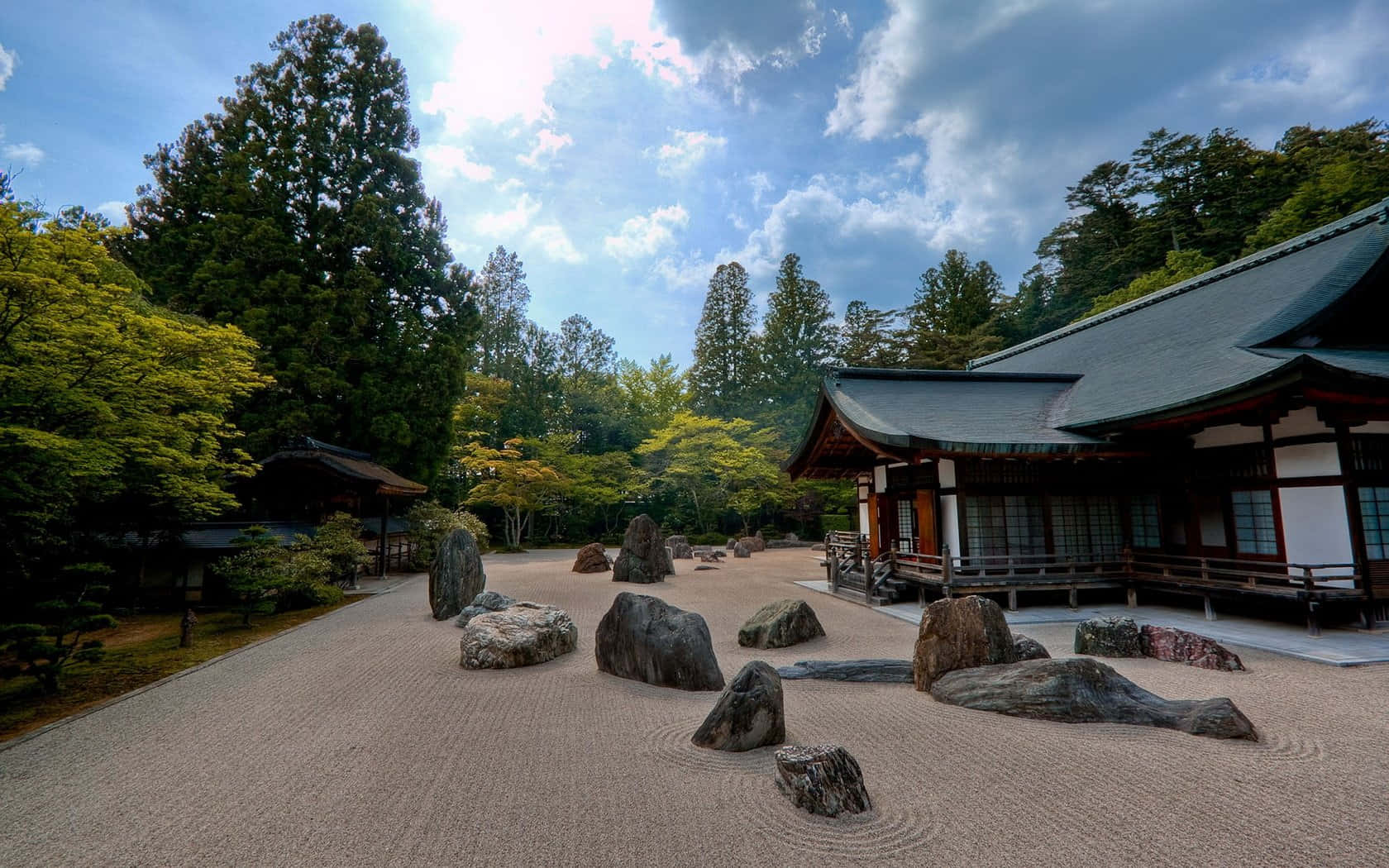 Samurai Garden 桌布 壁紙 — 一個寧靜的日本寺廟庭院，有耙過的碎石和長滿苔蘚的樹木，天空部分多雲。