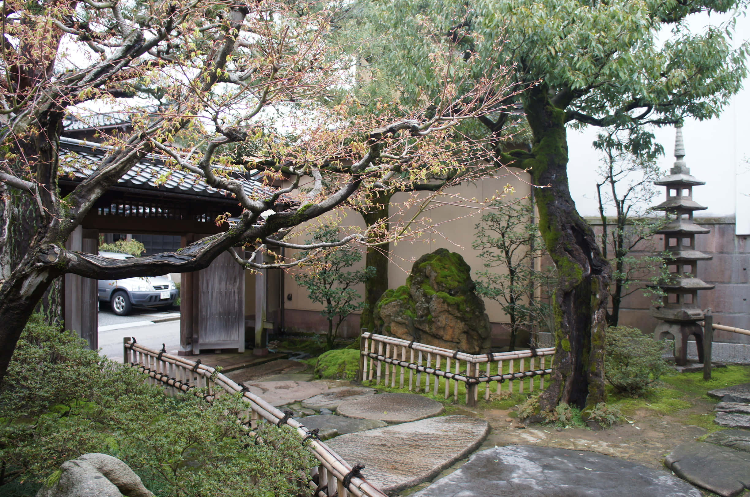 Samurai Garden 桌布 壁紙 — 一個寧靜的日本花園，有長滿青苔的石頭、蜿蜒的小徑、古樹和一座石塔，天空陰沉。
