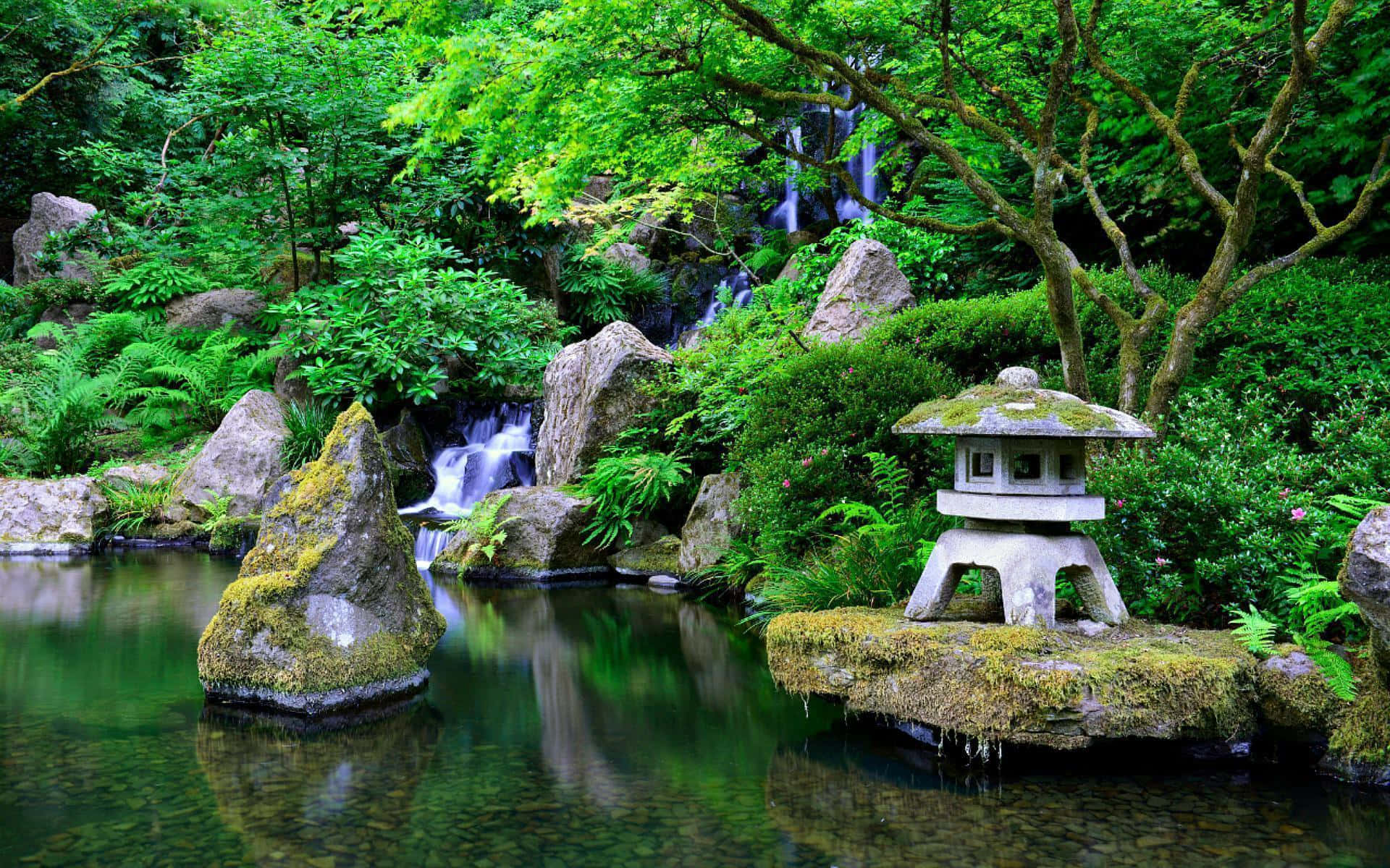 Samurai Garden 桌布 壁紙 — 一個寧靜的日本花園池塘，有長滿青苔的石燈籠、層疊瀑布和茂密的綠色樹葉倒映在平靜的水面上。