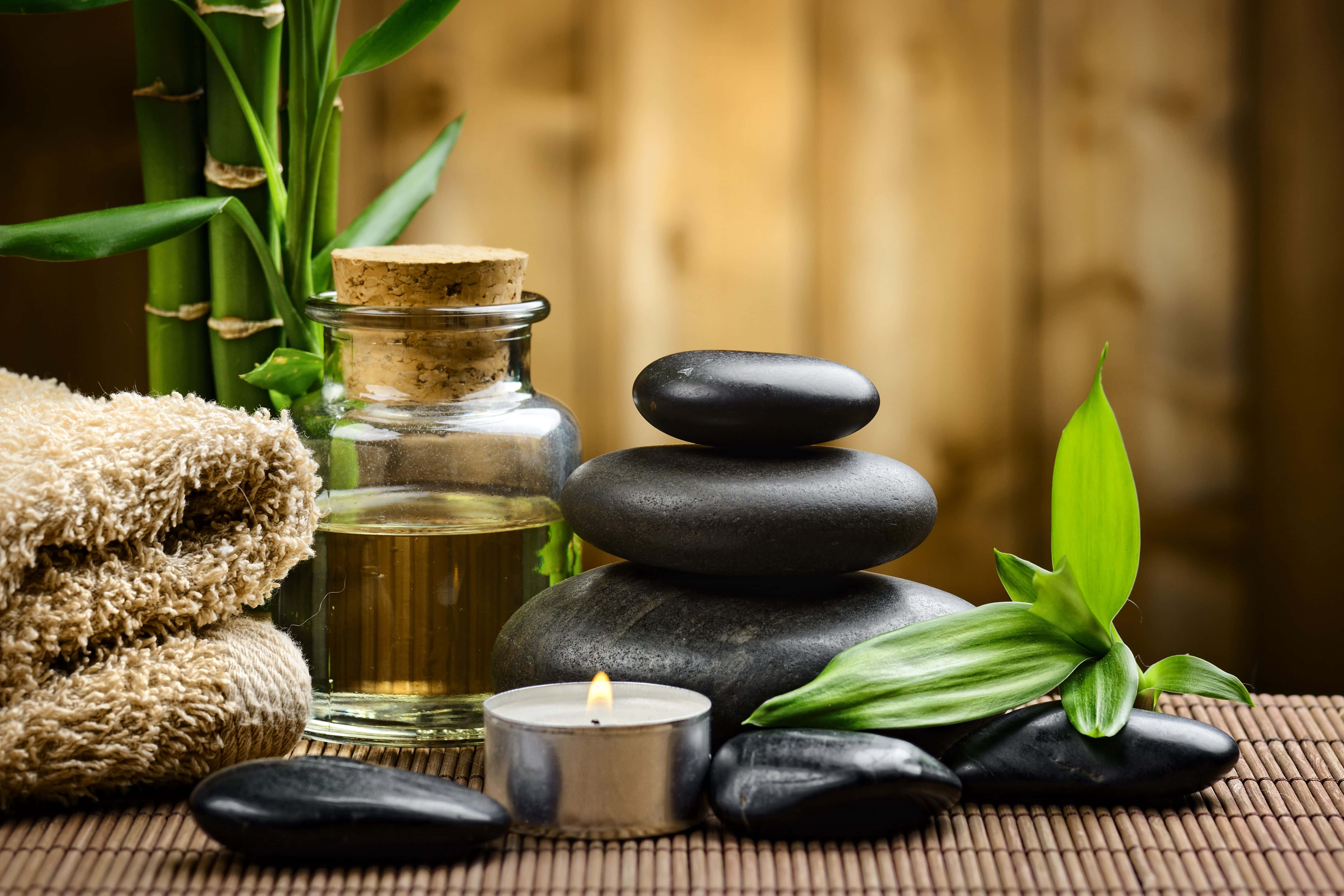 Spa Treatments 桌布 壁紙 — 一個寧靜的水療佈置，包括疊放的黑石、點燃的蠟燭、竹葉和一個玻璃瓶的油放在編織墊上。