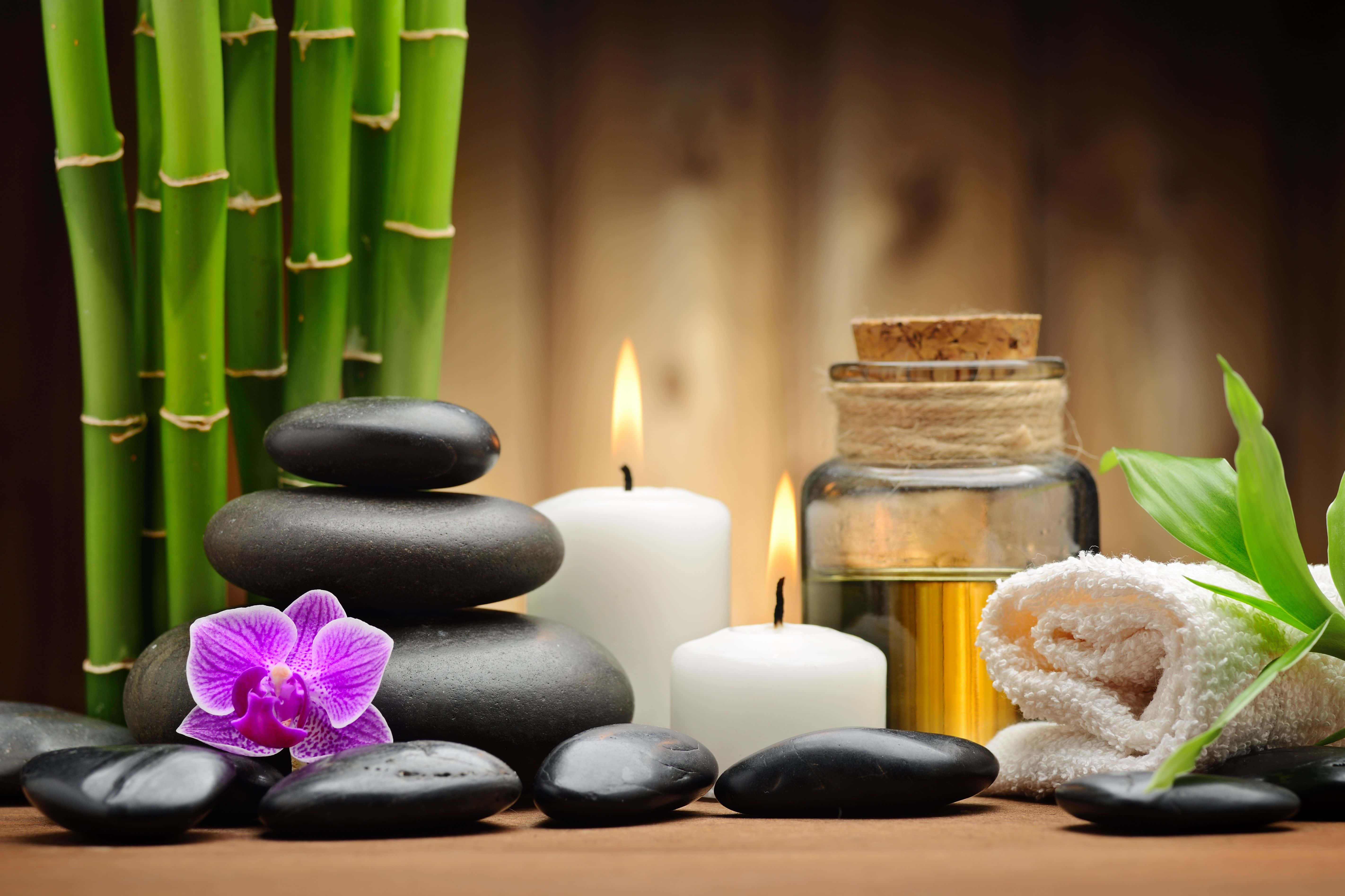 Spa Treatments 桌布 壁紙 — 一個寧靜的水療設置，包括疊放的黑石、紫色蘭花、點燃的蠟燭、竹子和木質表面上的捲毛巾。