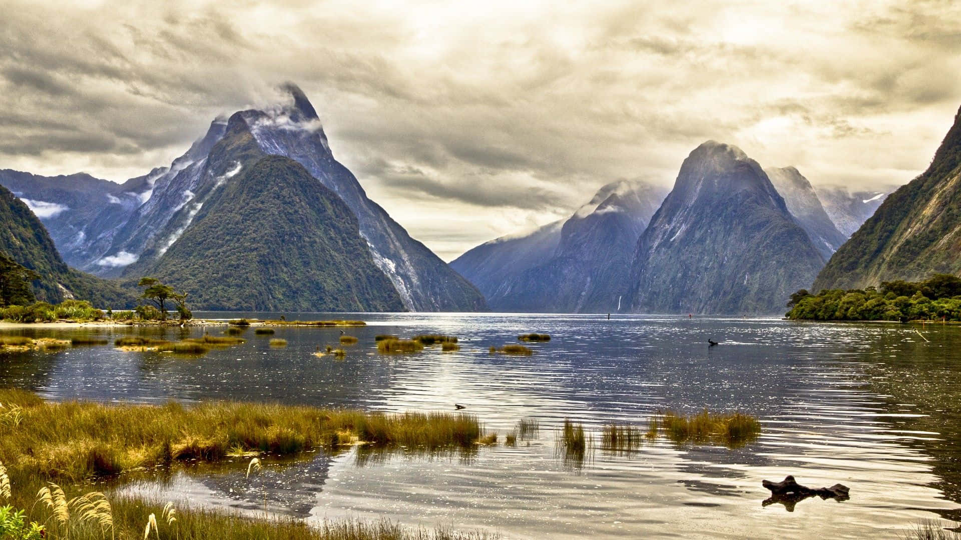 New Zealand 桌布 壁紙 — 一個寧靜的湖泊倒映著高聳的雪山，天空多雲，金光閃耀，氣氛壯麗。