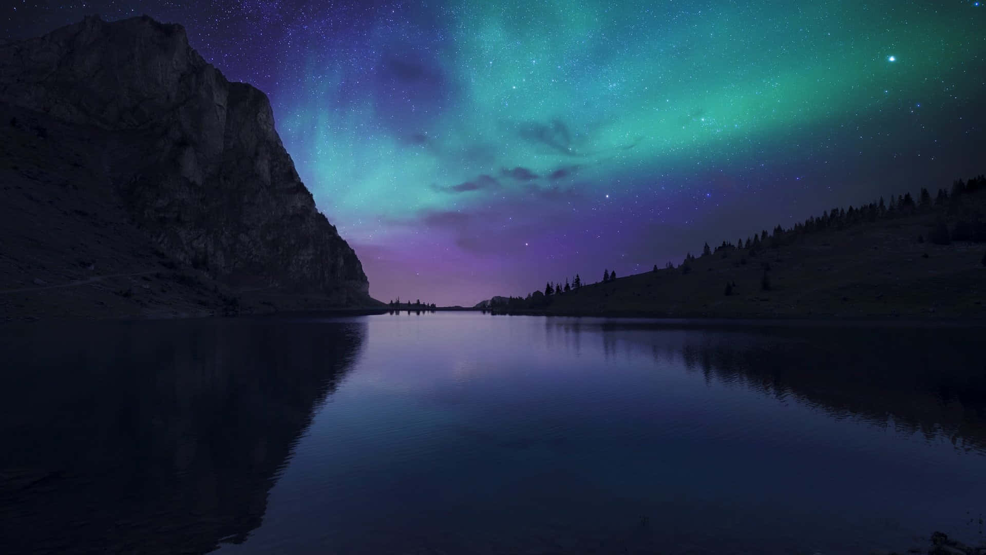 Ambience 桌布 壁紙 — 一個寧靜的湖泊映照出在星空和岩石懸崖上方舞動的鮮豔綠色和紫色北極光。