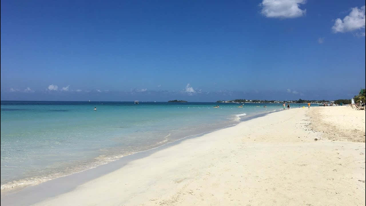 Jamaican Beach 桌布 壁紙 — 一個寧靜的熱帶海灘，有白色沙灘、碧綠海水和點綴著蓬鬆雲朵的清澈藍天。