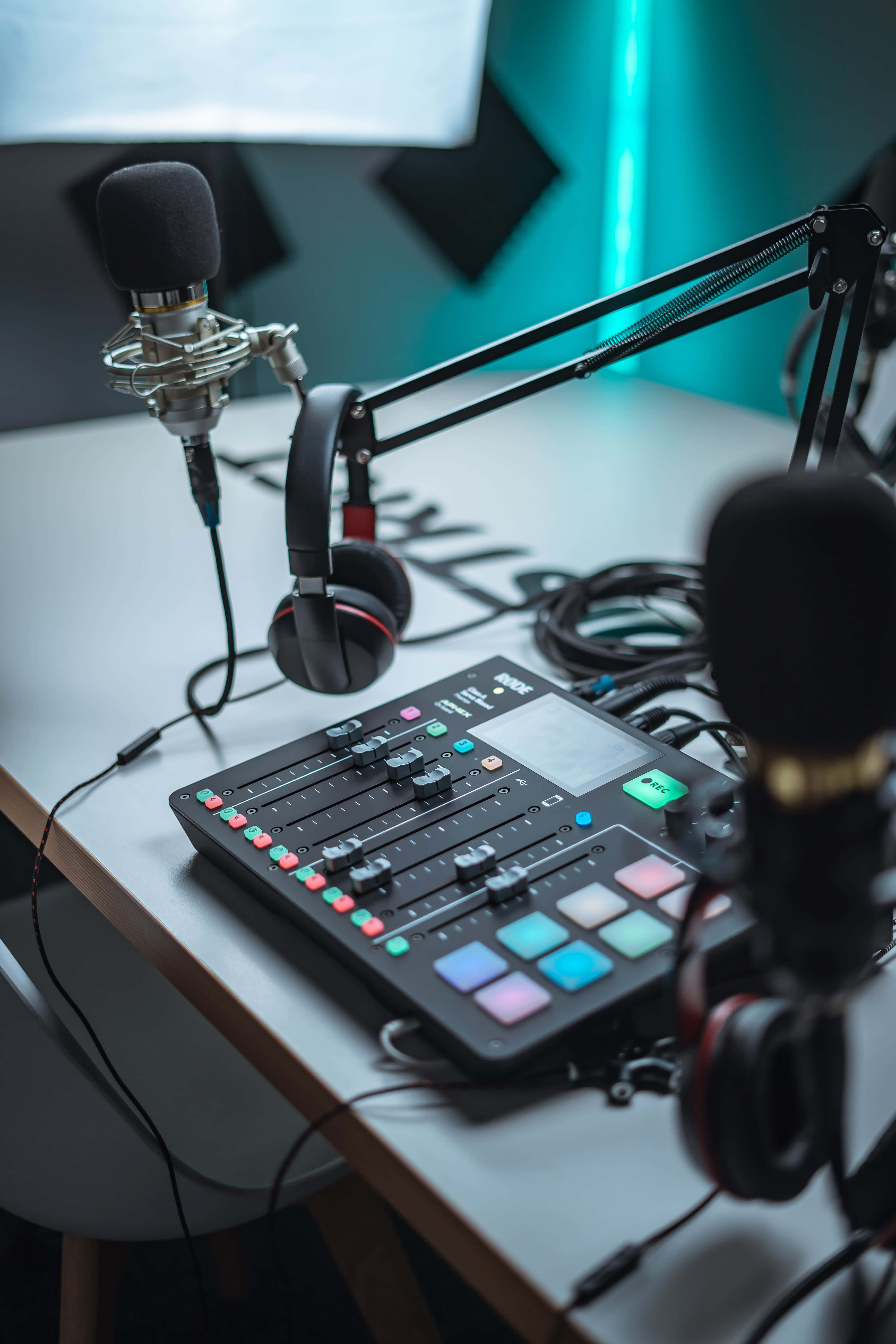 Podcasts 桌布 壁紙 — 一個專業的播客工作室設置，配有麥克風、耳機和音頻混音器，在冷藍色燈光下的桌子上。