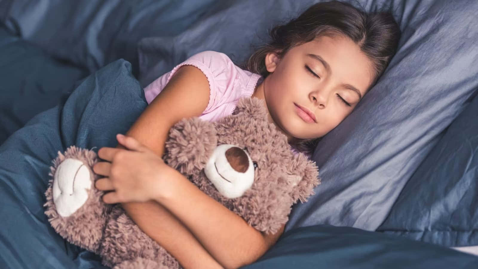 Sleep 桌布 壁紙 — 一個小女孩在深藍色床單上抱著毛絨絨的棕色泰迪熊安然入睡。