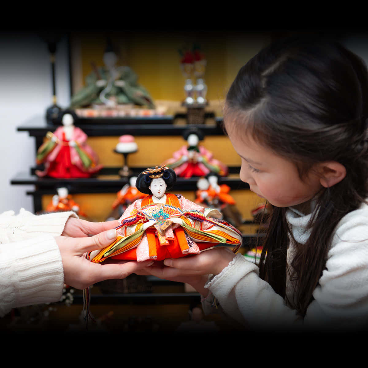 Dolls 桌布 壁紙 — 一個小女孩專注地凝視著一個由成人雙手溫柔捧著的傳統日本娃娃，背景是柔和模糊的神社。
