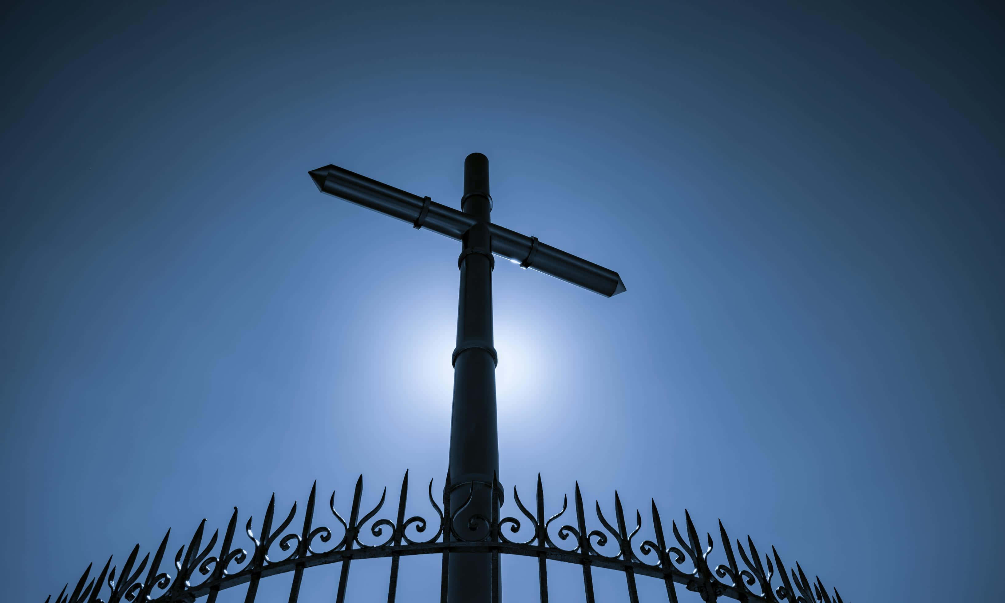 Religious Easter 桌布 壁紙 — 一個尖銳的黑色十字架矗立在華麗的大門上，背景是深藍色的暮色天空，太陽在後面發光。