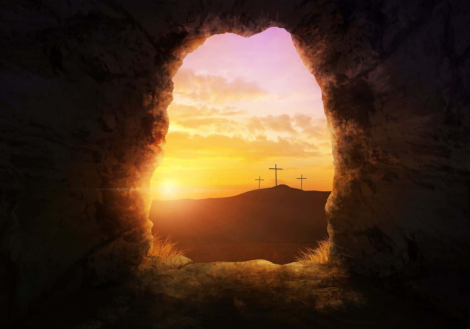 Gospel 桌布 壁紙 — 一個岩石洞穴入口框住咗一個日出，山丘上有三個十字架嘅剪影襯住金色雲層。