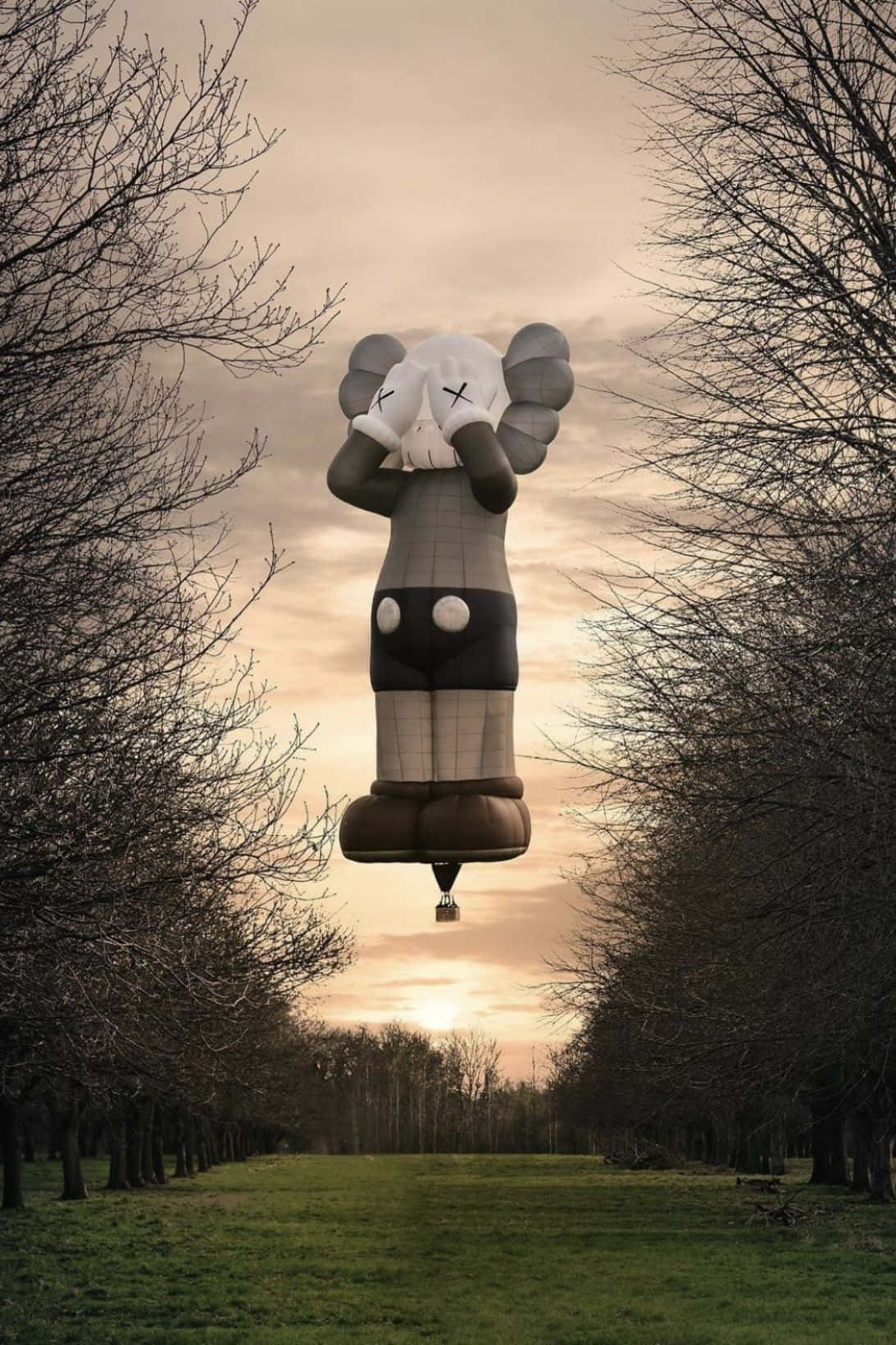 Kaws Holiday 桌布 壁紙 — 一個巨大的KAWS氣球雕塑在日落時分寧靜地漂浮在一排排光禿禿的樹木之間。