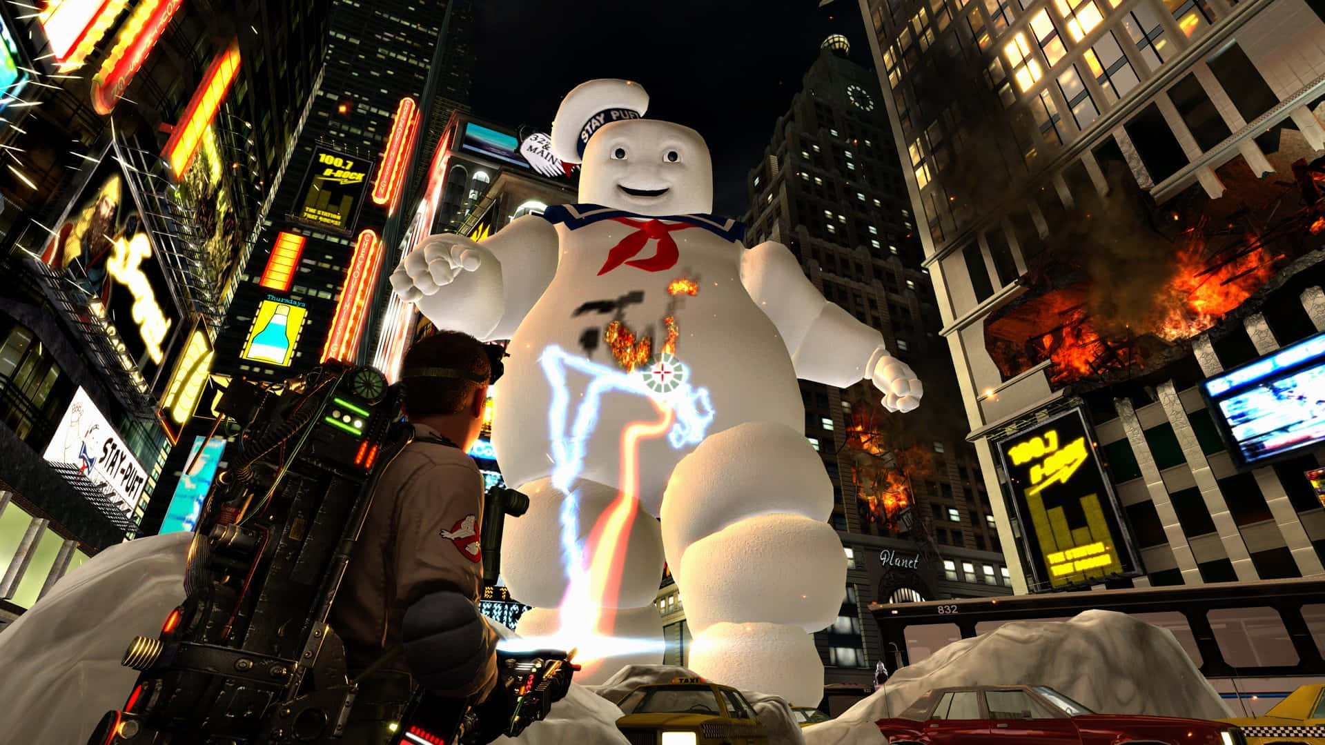 Ghostbusters 桌布 壁紙 — 一個巨大的Stay Puft棉花糖人聳立在積雪的紐約街道上，一名捉鬼敢死隊員在燃燒的建築物和霓虹燈招牌中將質子背包對準它。