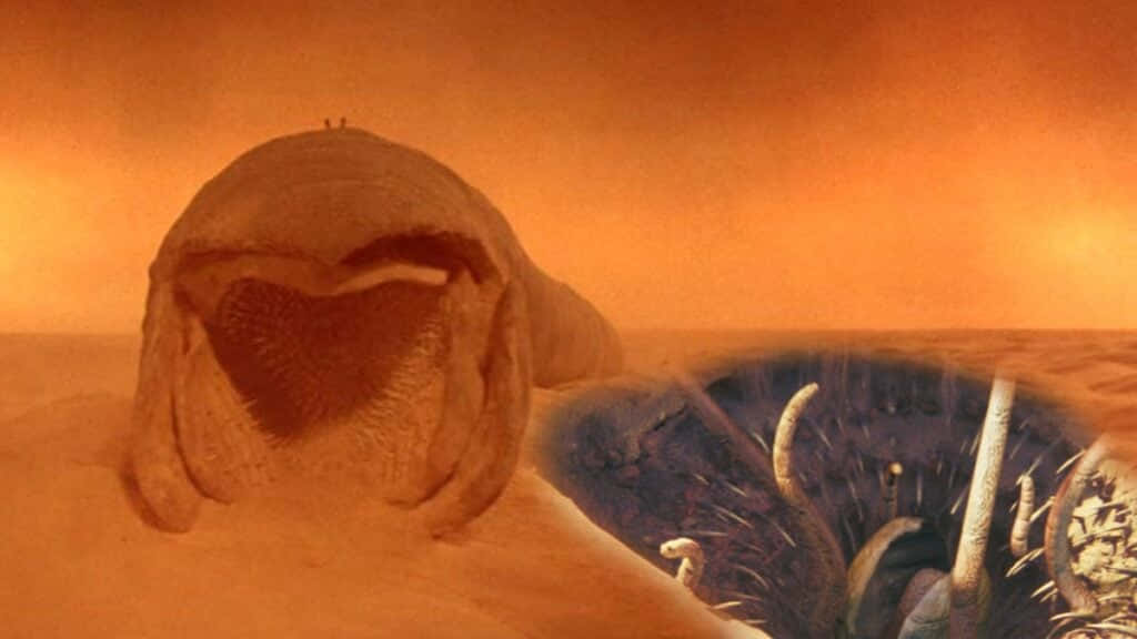 Sarlacc 桌布 壁紙 — 一個巨大的外星生物，帶有紋理外殼和張開的大嘴，從橙色的沙漠中出現，天空朦朧。