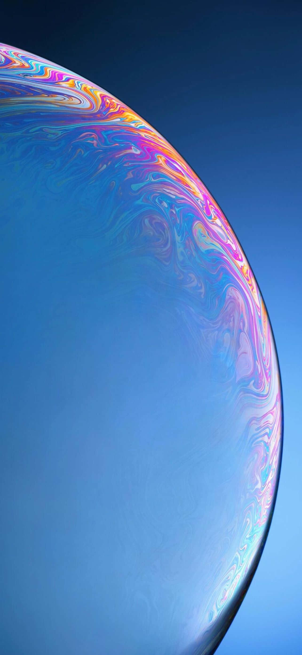 藍色 iPhone 桌布 壁紙 — 一個巨大的彩虹色肥皂泡在清澈的藍天中漂浮，邊緣呈現旋轉的彩虹色。