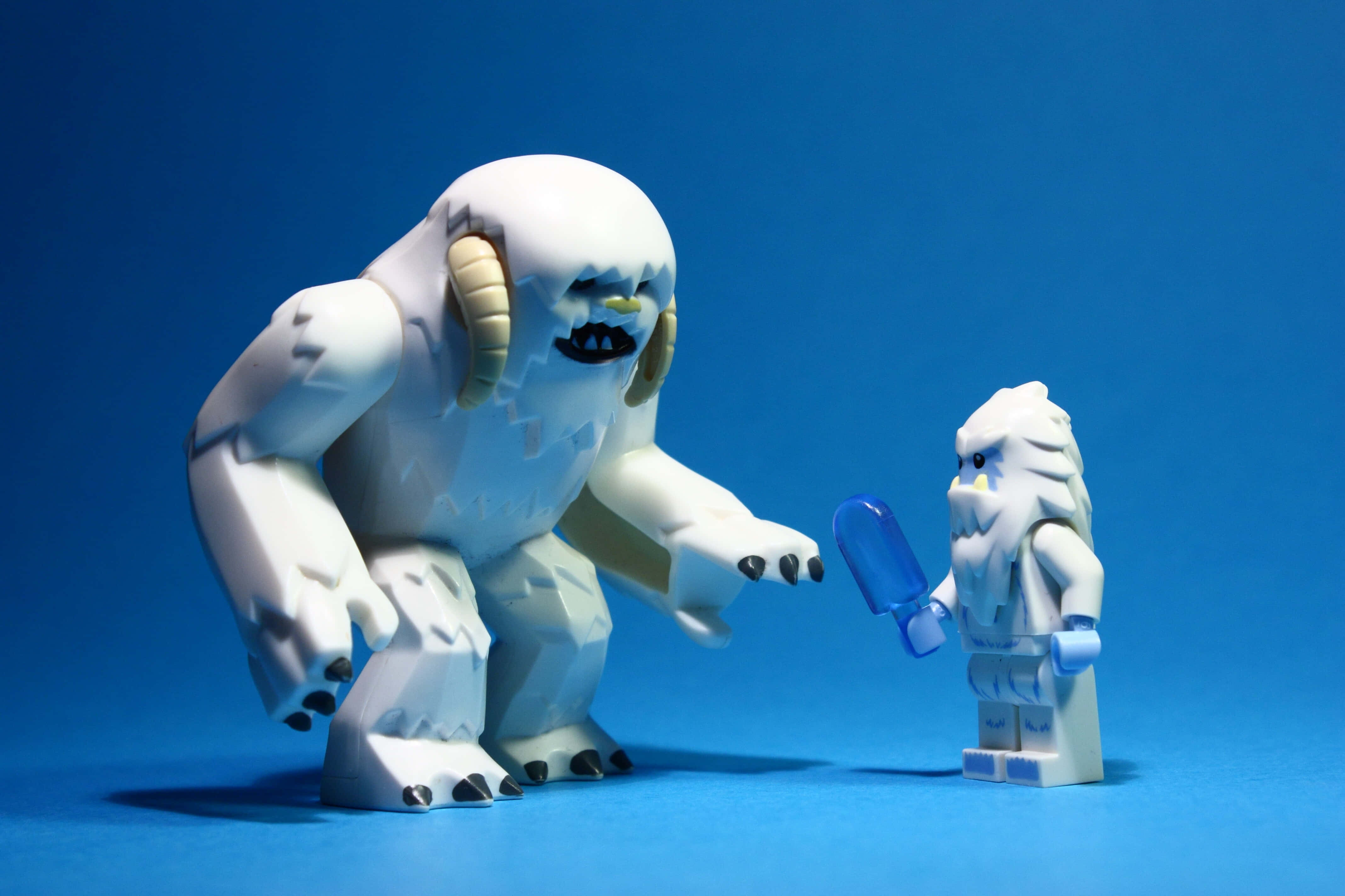 Wampa 桌布 壁紙 — 一個巨大的白色LEGO雪人聳立在一個較小的白色LEGO人仔上方，該人仔手持藍色冰棒，背景為純藍色。