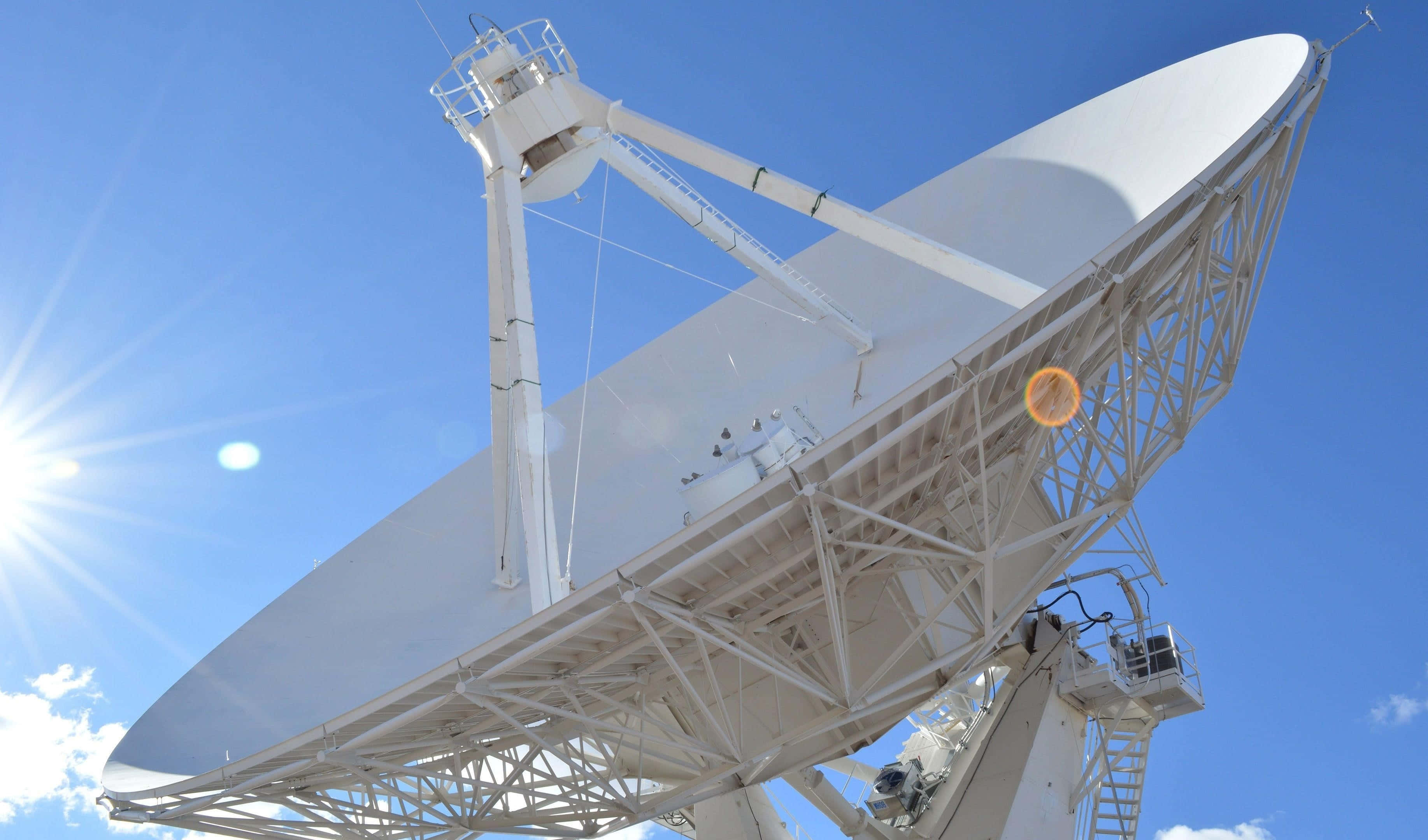 Satellite 桌布 壁紙 — 一個巨大的白色無線電望遠鏡碟形天線在明亮的陽光下閃耀，背景是清澈的藍天，帶有鏡頭光暈。
