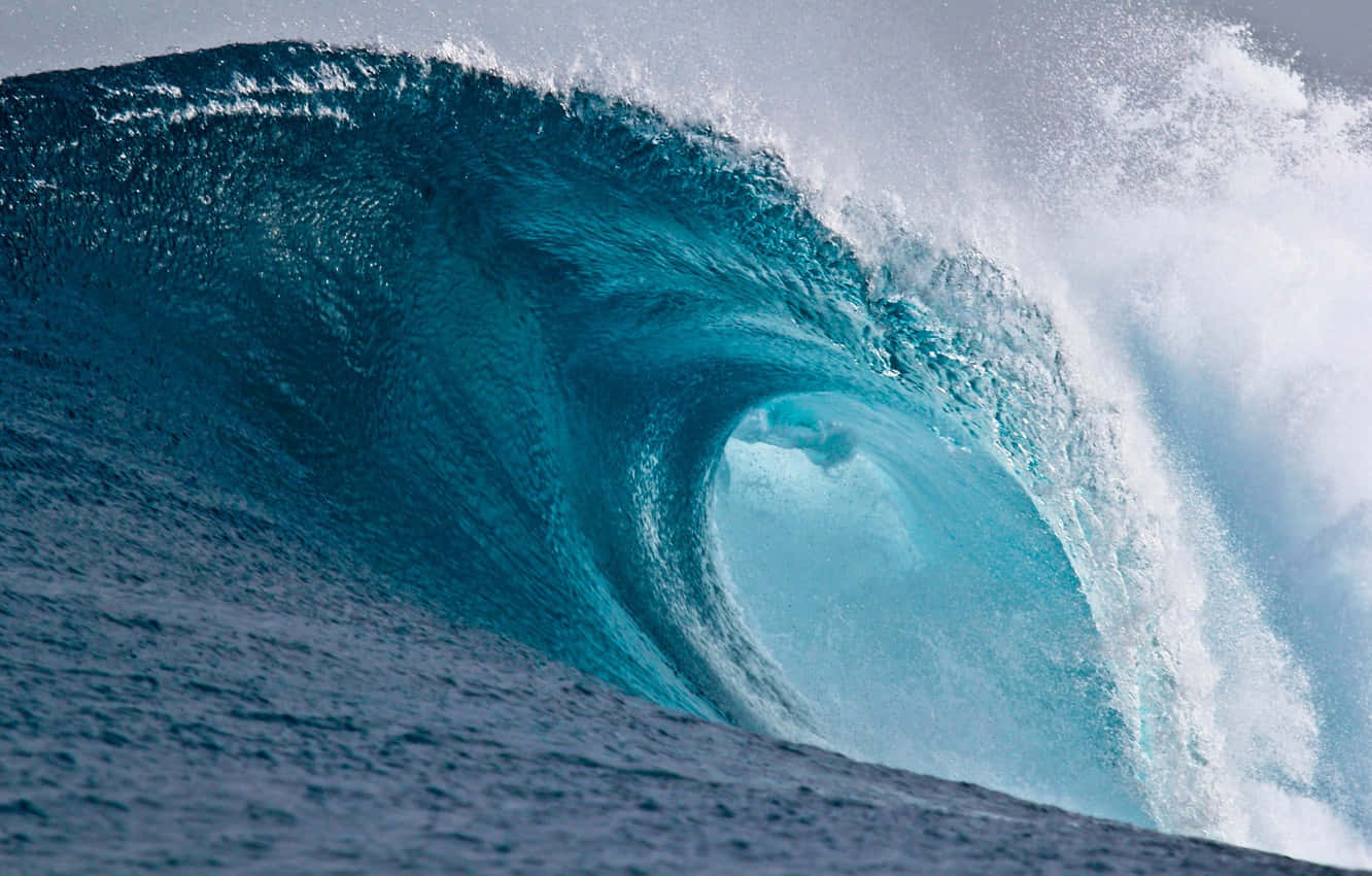 waves 桌布 壁紙 — 一個巨大的藍綠色海浪捲成一個完美的筒狀，伴隨著泡沫般的白色水花，映襯著灰色的天空。