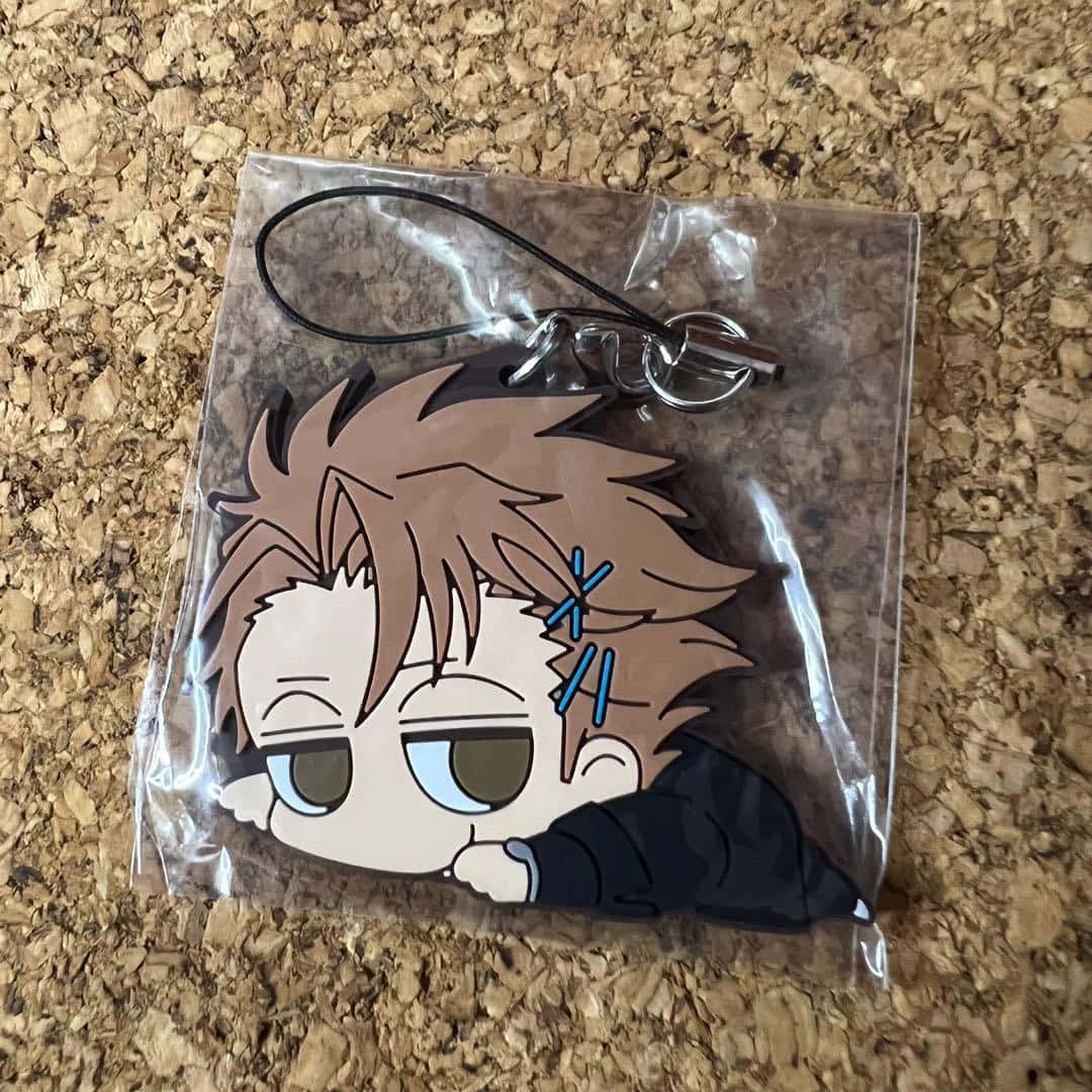 Shusei Kagari 桌布 壁紙 — 一個帶有凌亂棕色頭髮和疲倦眼睛的Q版動漫角色鑰匙圈，放在軟木表面上的透明塑料中。