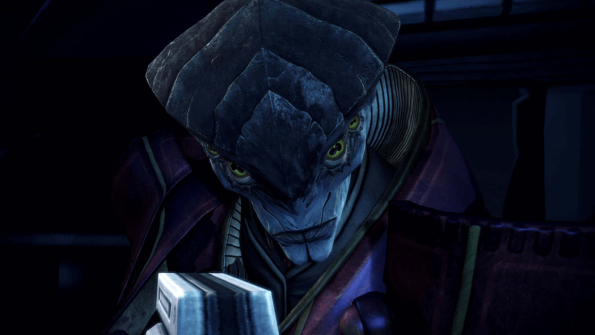 Mass Effect Javik 桌布 壁紙 — 一個帶有發光黃色眼睛和深藍色皮膚的威脅性外星人，在昏暗的房間裡專注地凝視著一個發光的裝置。