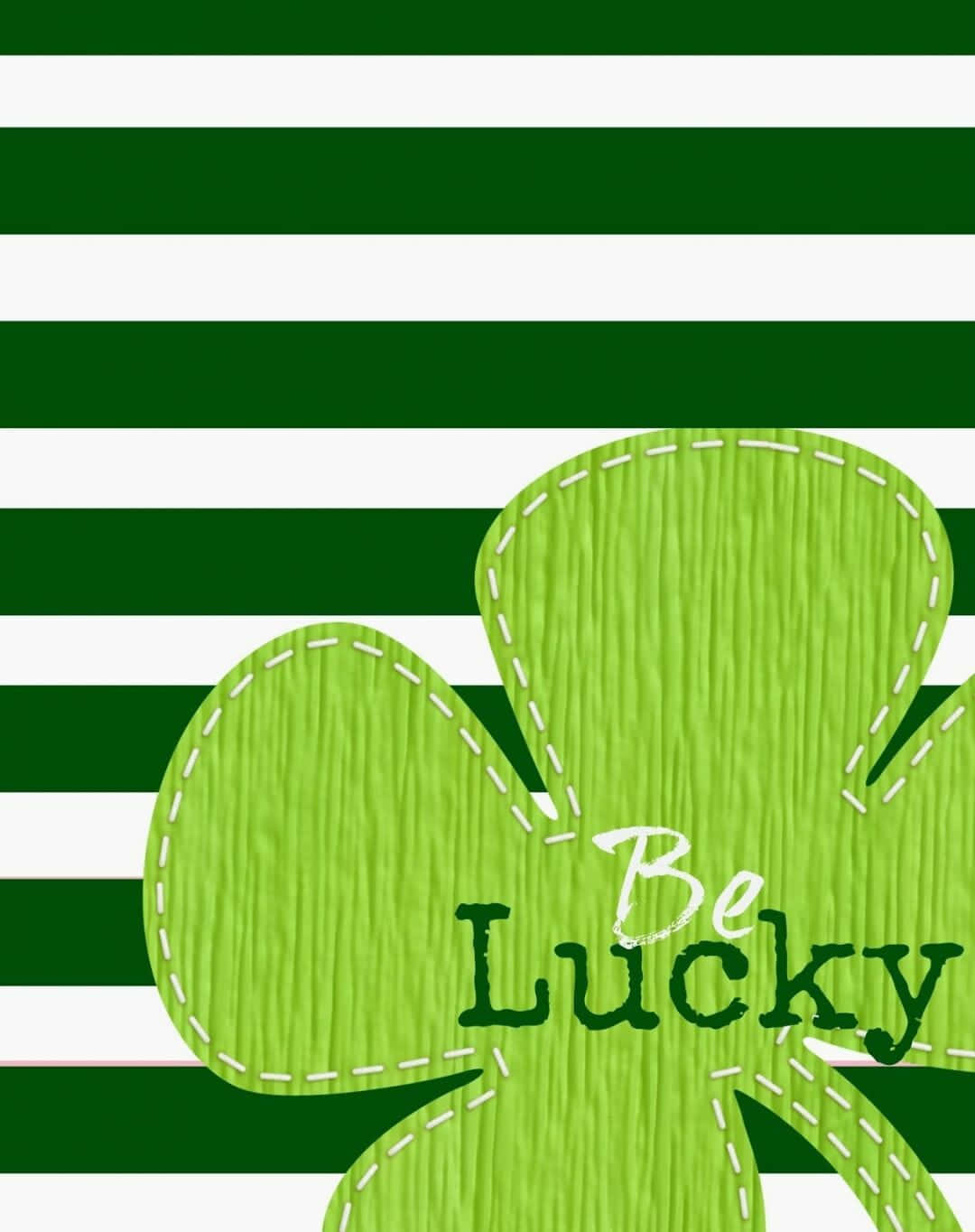 St Patrick's Day 桌布 壁紙 — 一個帶有白色縫線和「Be Lucky」文字的亮綠色三葉草漂浮在醒目的綠色和白色水平條紋上。