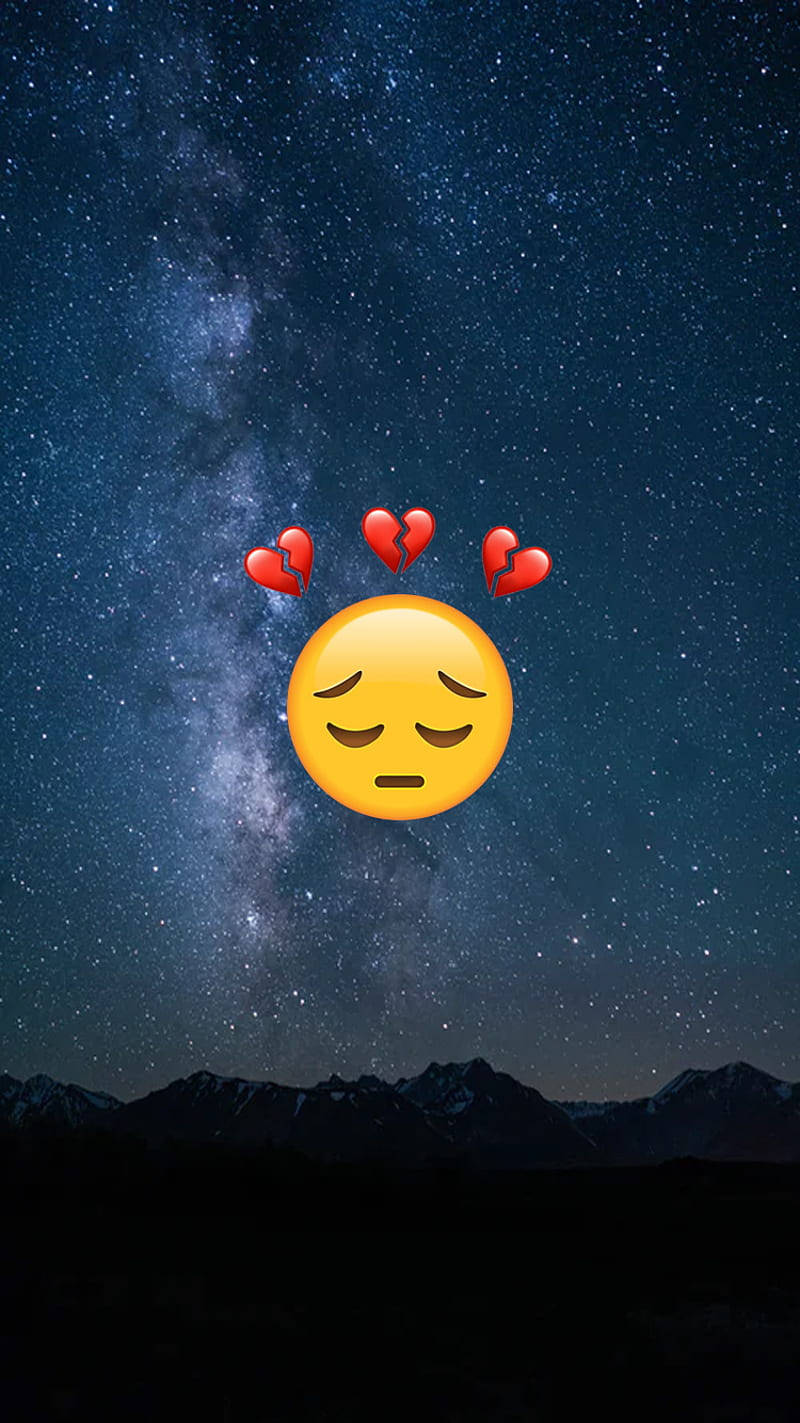 悲傷表情符號帶有破碎心心，襯托著星空夜空和山脈輪廓。 — 心碎 GIF 壁紙