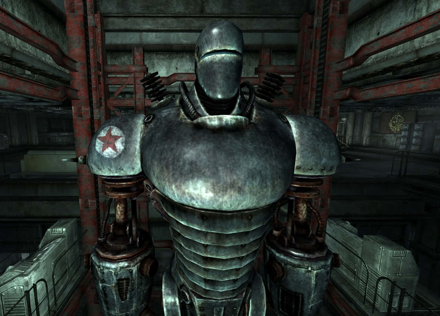 Liberty Prime 桌布 壁紙 — 一個帶有紅色星星標誌的高聳金屬機械人，站在一個有生鏽金屬橫樑的昏暗工業倉庫中。
