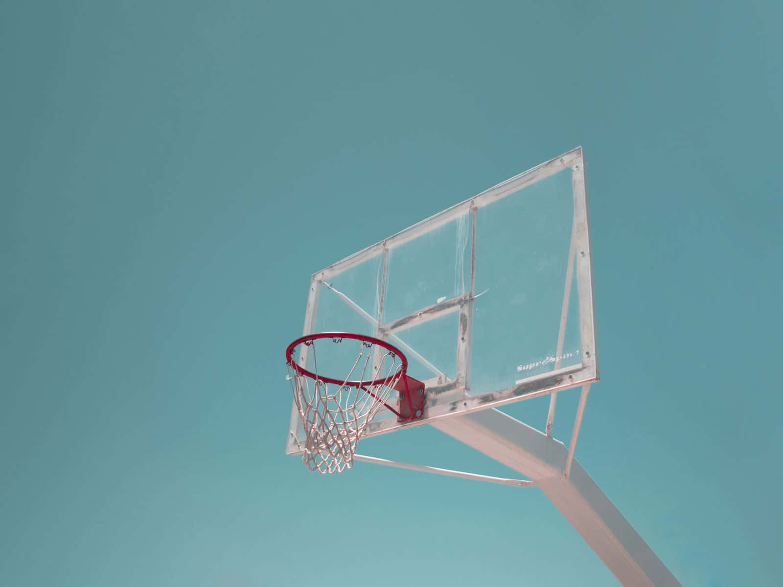 Minimalist Sports 桌布 壁紙 — 一個帶有紅色籃框和透明籃板的籃球架，矗立在純色青綠色的天空下。