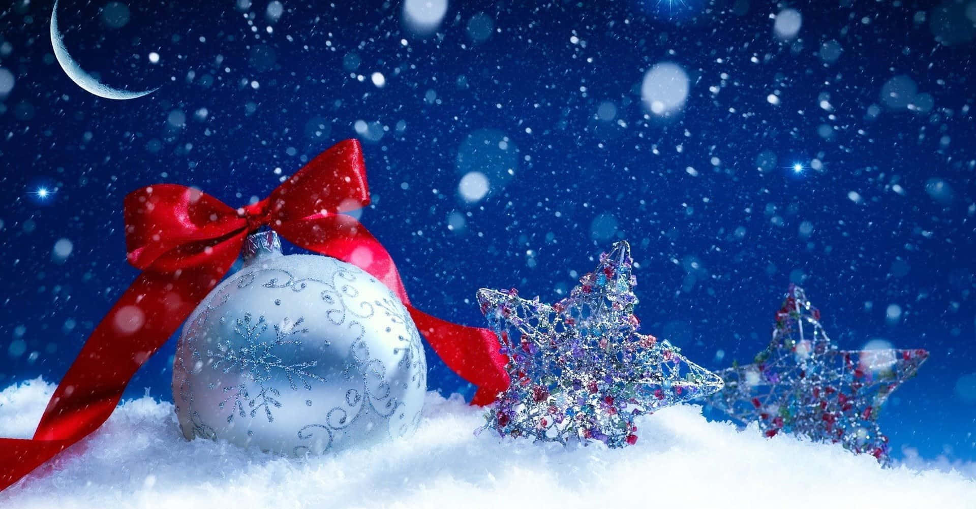 Winter Christmas 桌布 壁紙 — 一個帶有紅色蝴蝶結和閃爍星星的銀色裝飾品，躺在新月和飄雪下的雪地中。