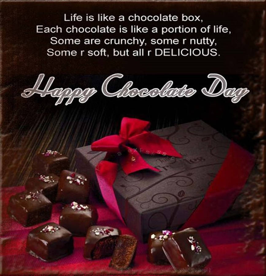 Chocolate Day 桌布 壁紙 — 一個帶有紅色蝴蝶結的黑朱古力禮盒，旁邊放著各式朱古力，放在一塊印有勵志語句的紅布上。