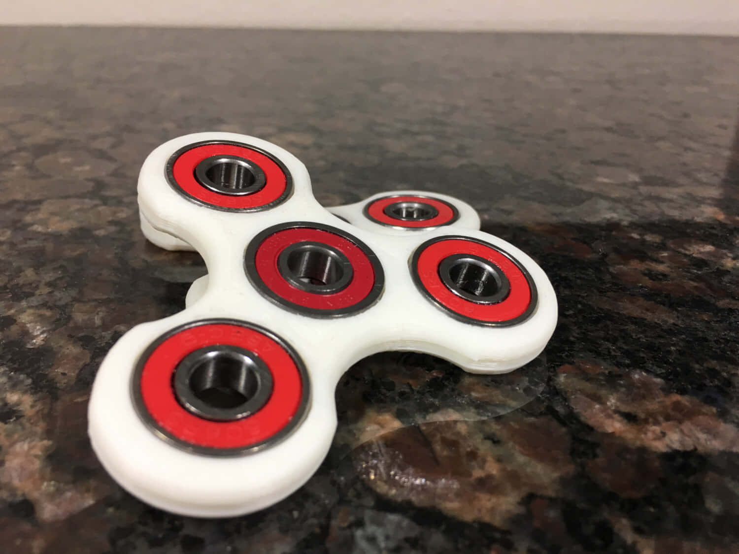 Fidget 桌布 壁紙 — 一個帶有紅色軸承的白色指尖陀螺，放置在深色斑點檯面上。