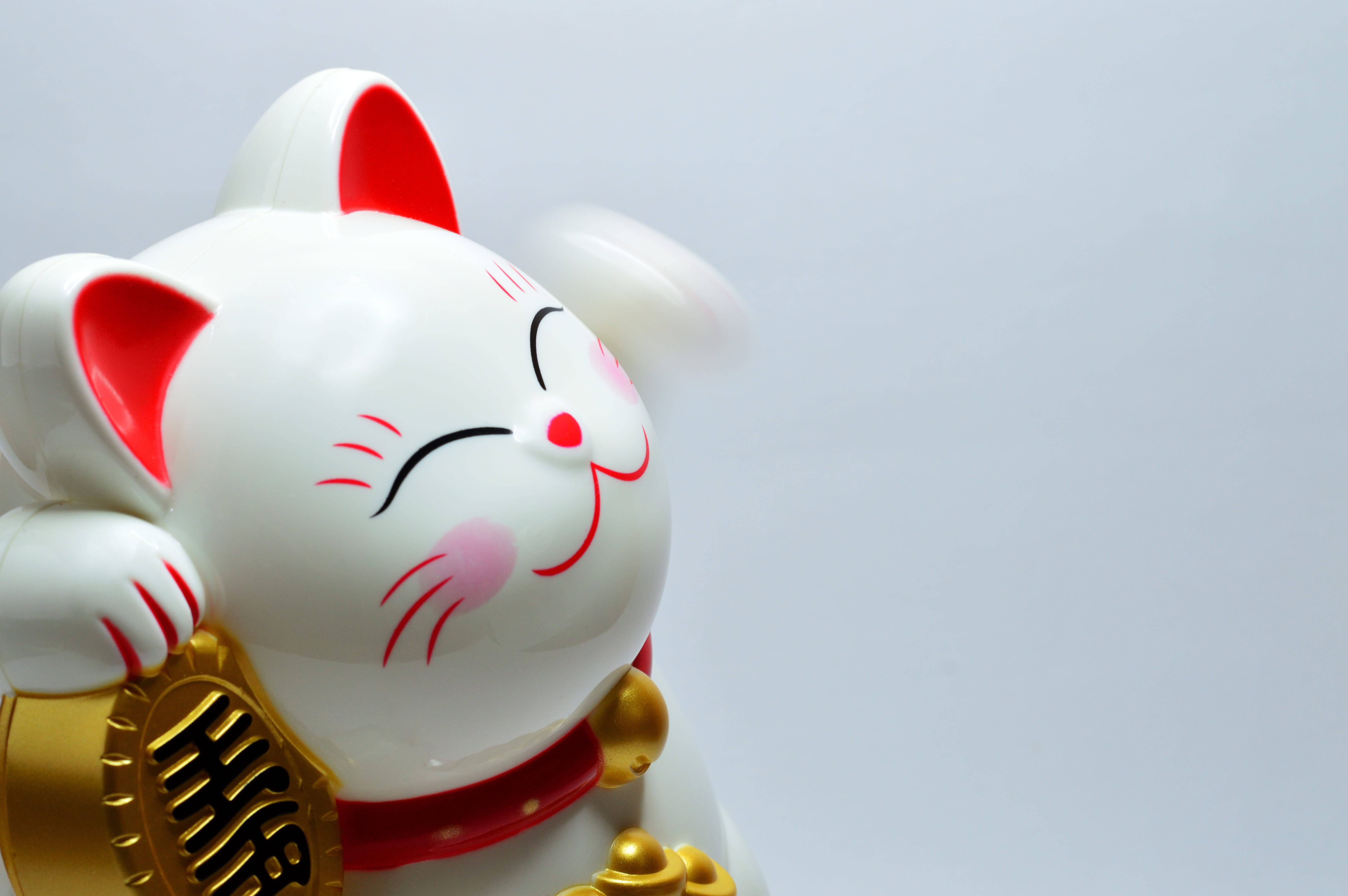 Japanese 桌布 壁紙 — 一個帶有紅色點綴和金幣的光澤白色招財貓公仔，在純白色背景上保持微笑姿勢。