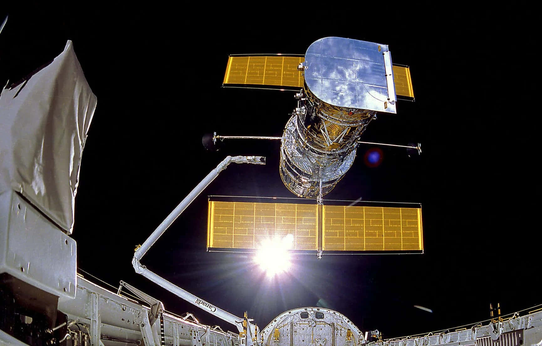 Hubble Space Telescope 桌布 壁紙 — 一個帶有金色太陽能板和反射機身的太空望遠鏡，在漆黑的太空虛空中懸浮，背後有明亮的太陽耀斑。