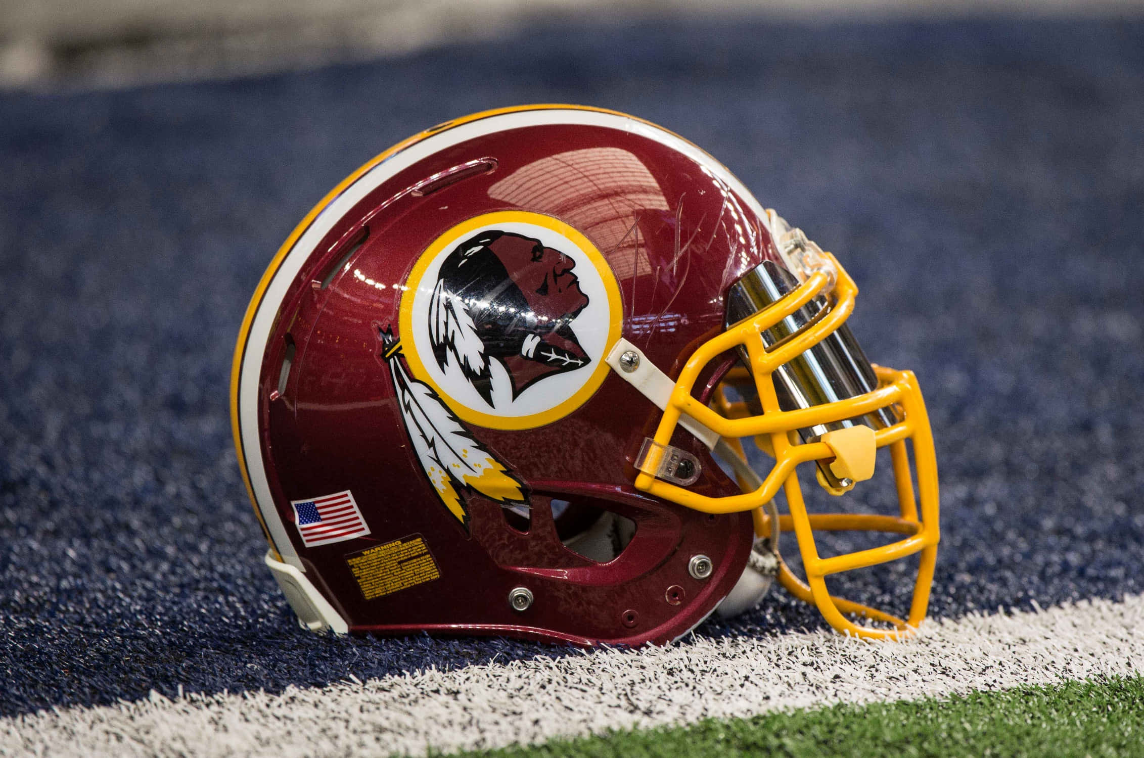 Washington Football 桌布 壁紙 — 一個帶有黃色面罩的栗色華盛頓足球隊頭盔，放在藍色草皮上，靠近白色碼線。