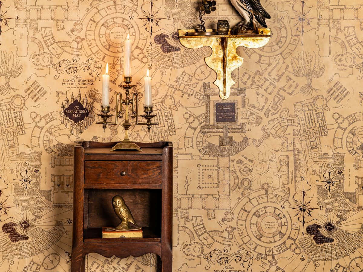 The Marauder's Map 桌布 壁紙 — 一個帶有黃銅貓頭鷹雕像和燭台的古董木櫃，矗立在覆蓋著複雜哈利波特劫盜地圖壁紙的牆前。